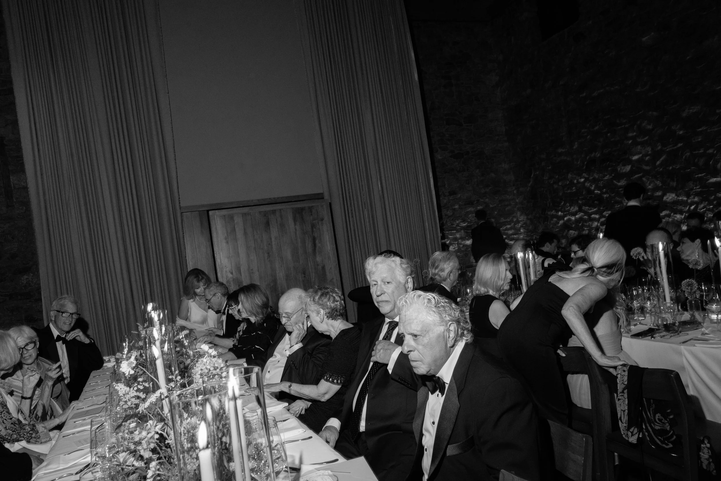 Black-and-white candid of family and guests gathered around the table during dinner.