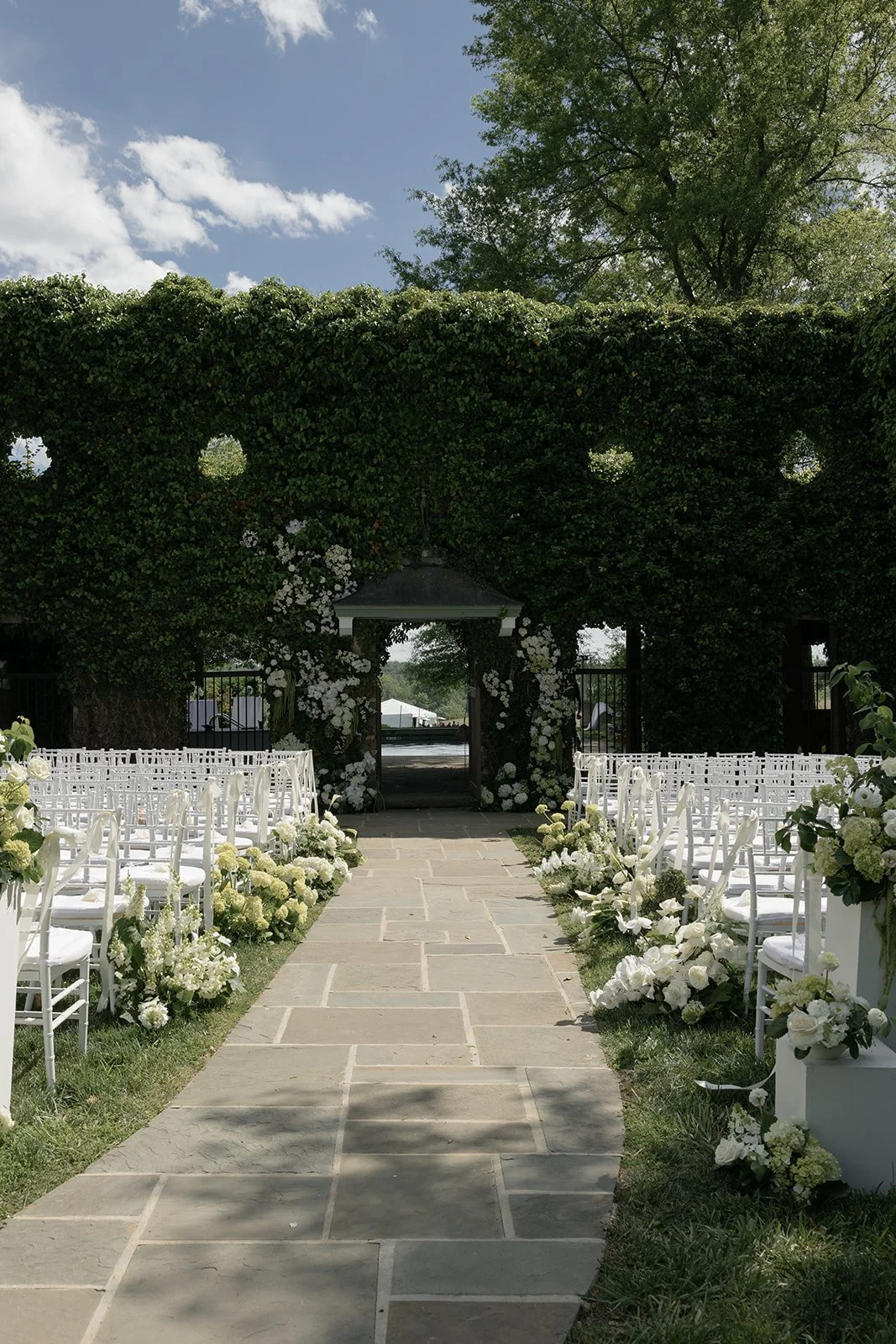 Goodstone Inn ceremony aisle framed by white flowers and greenery beneath a bright spring sky at Goodstone Inn.