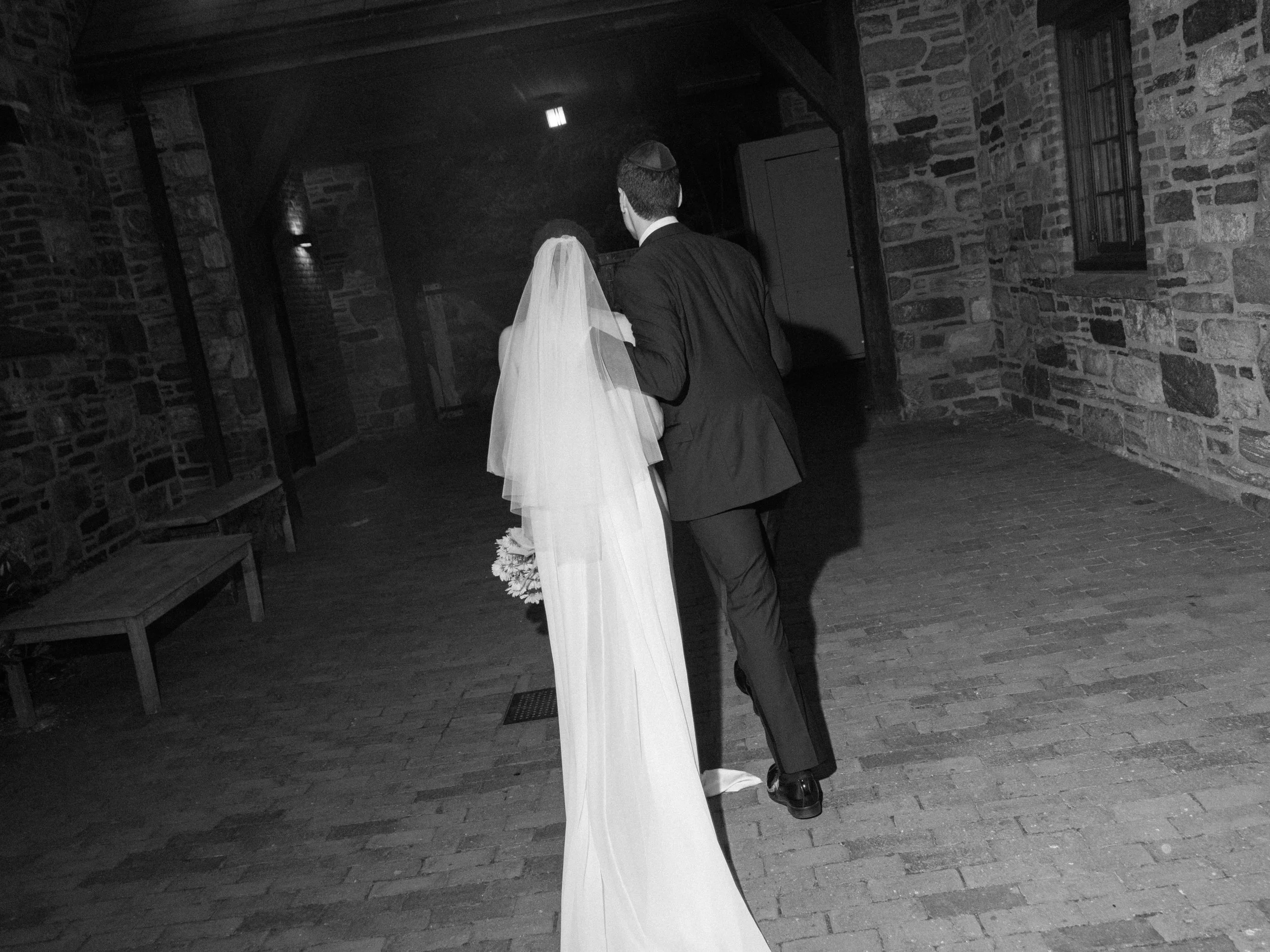 A timeless black and white candid capture of the bride and groom exiting their ceremony space with the bride's veil and wedding dress train trailing behind her. 