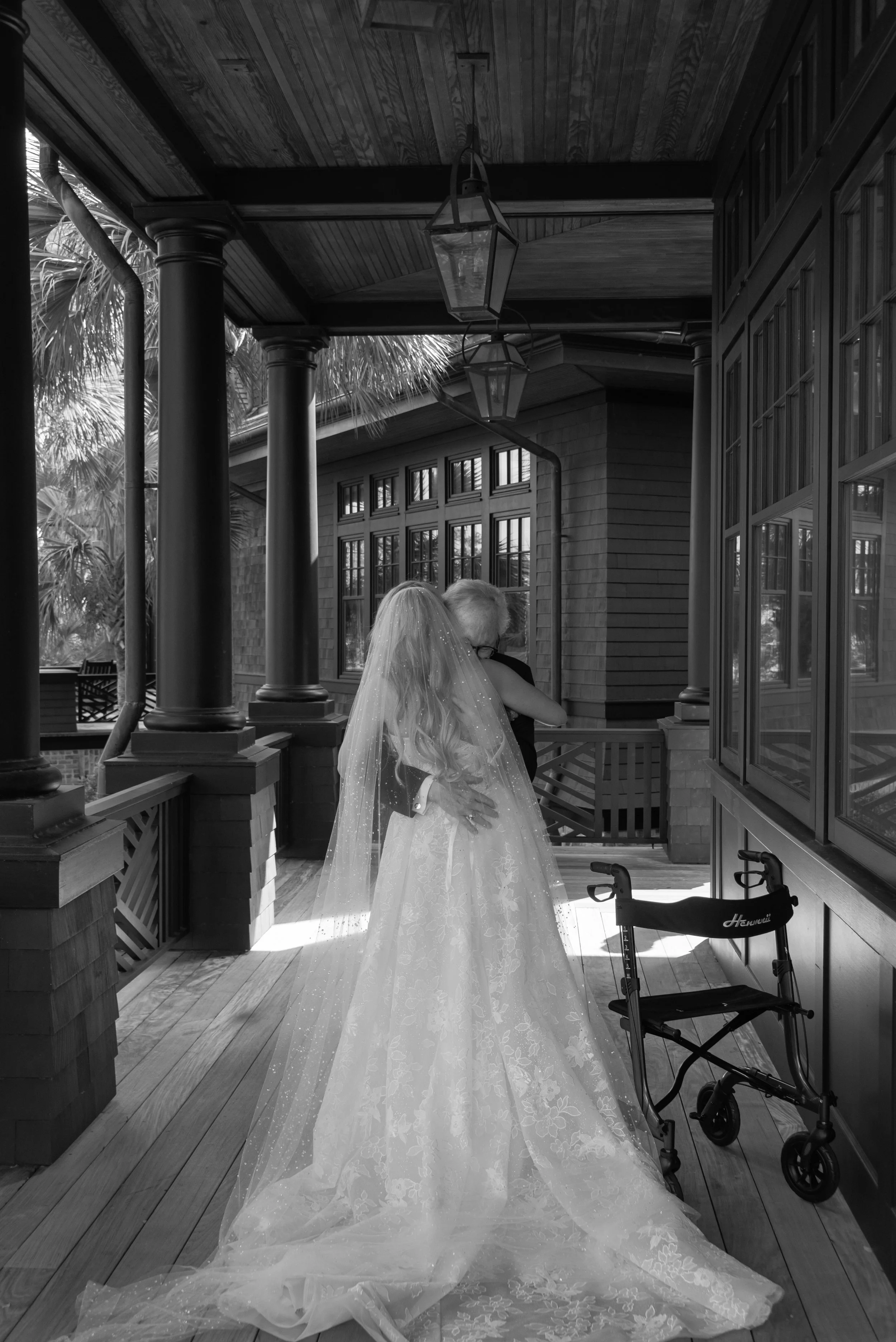 Black-and-white portrait of Katie hugging her father with her long veil trailing behind her.