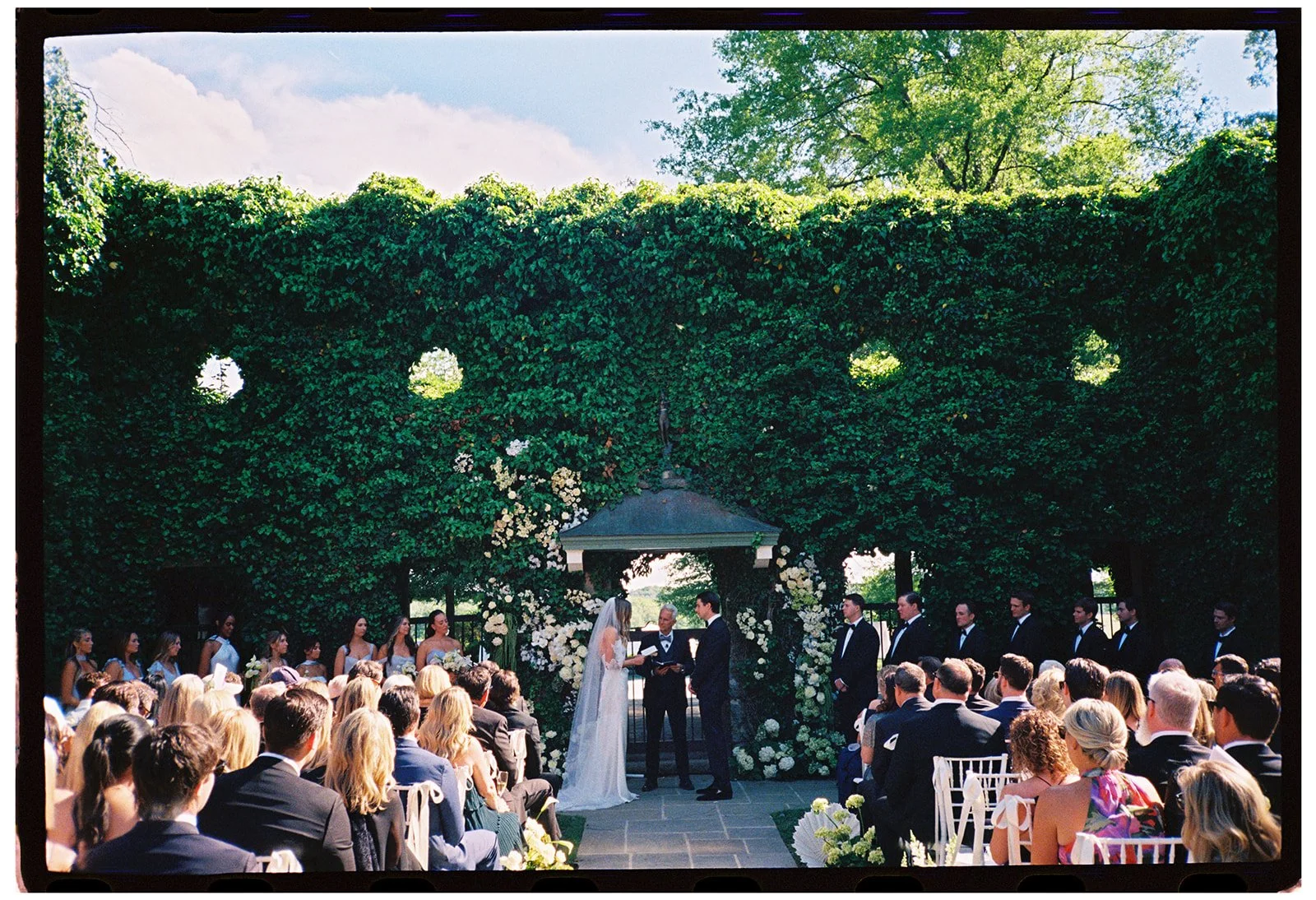 ide view of the outdoor Ivy Wall ceremony at Goodstone Inn surrounded by guests and lush greenery on 35mm film