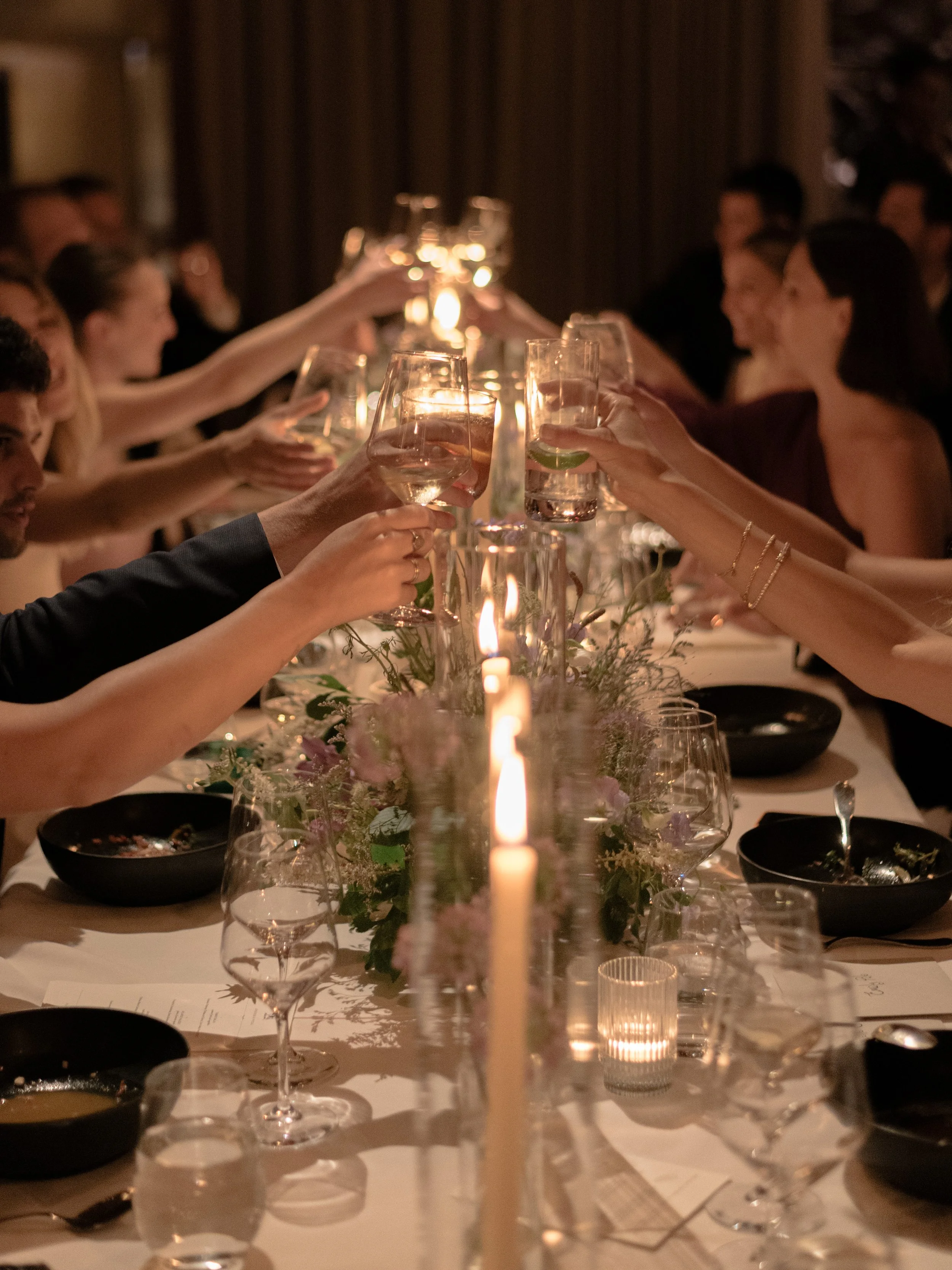Guests raise their glasses in a toast across the candlelit reception table.