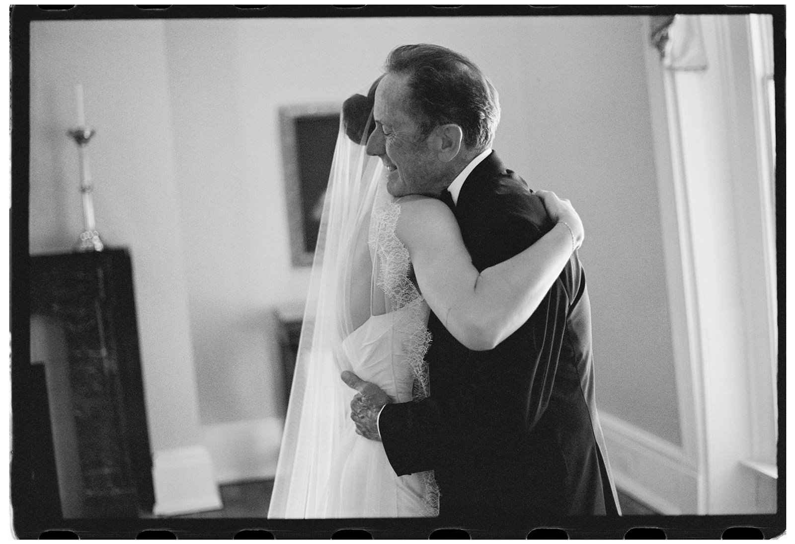 Black and white film wedding photograph of a bride embracing her father before her ceremony at Ravenswood Mansion, capturing an intimate family moment.