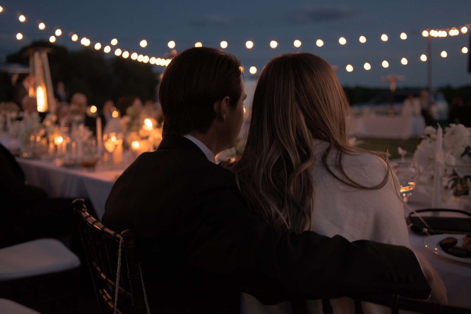 Bride and groom seated together at their outdoor dinner reception beneath string lights at Goodstone Inn.