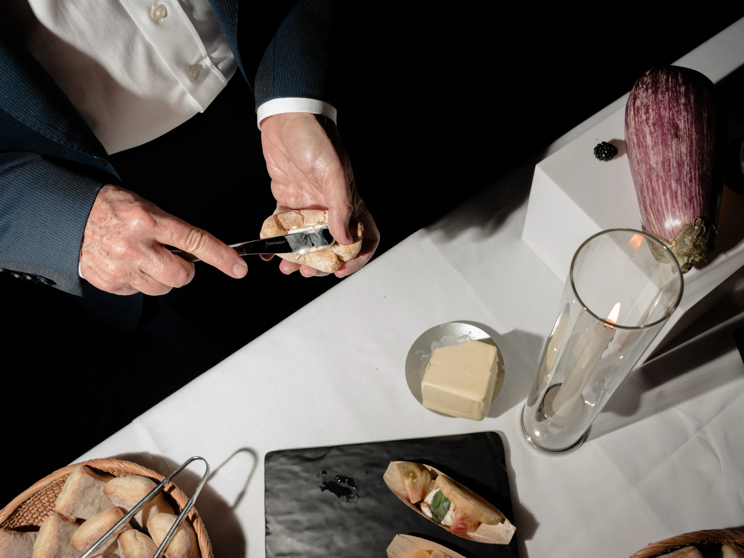 Hands buttering a dinner roll at the interactive rehearsal dinner food display table. 