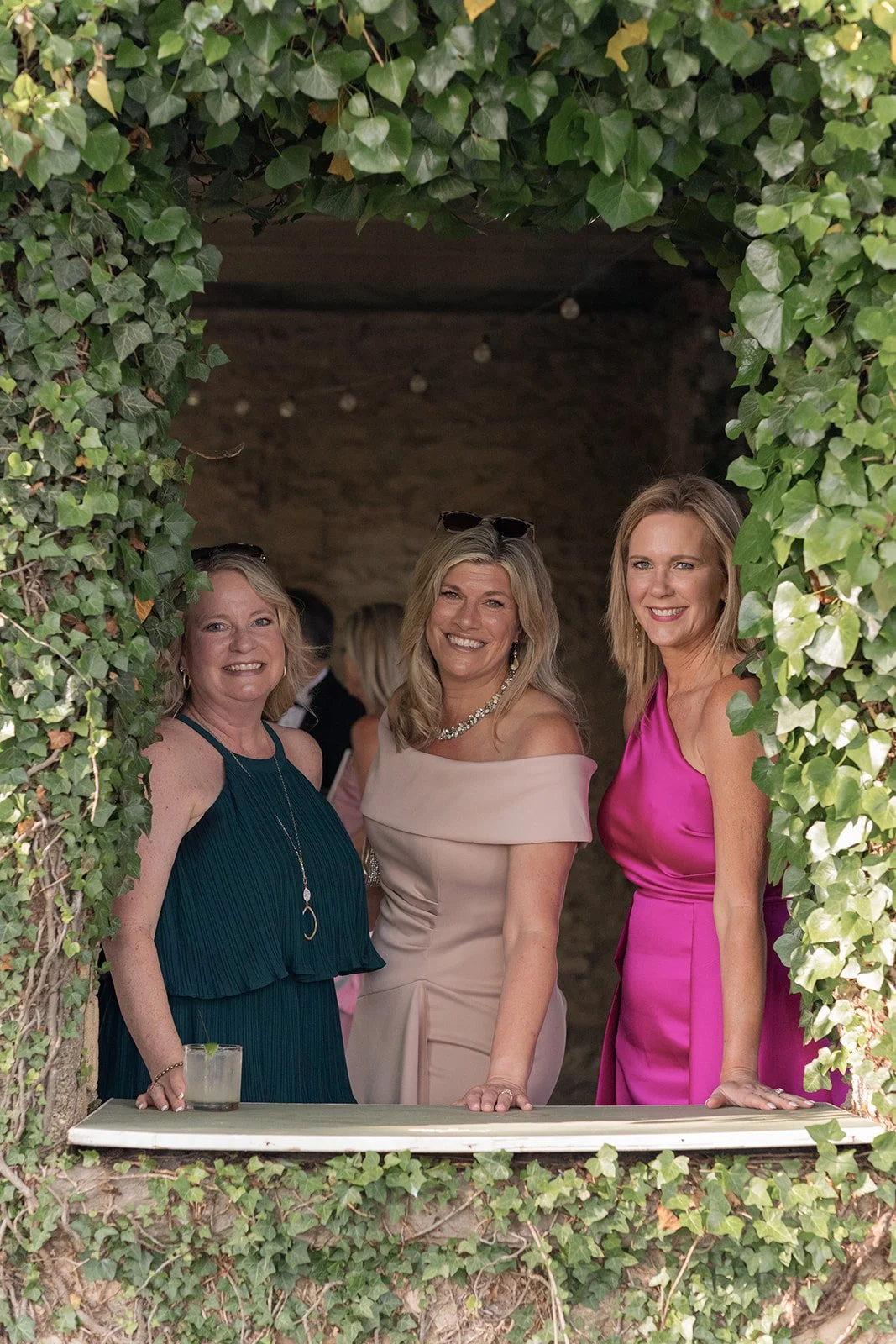 Three wedding guests in colorful formalwear posing together during cocktail hour at Goodstone Inn.