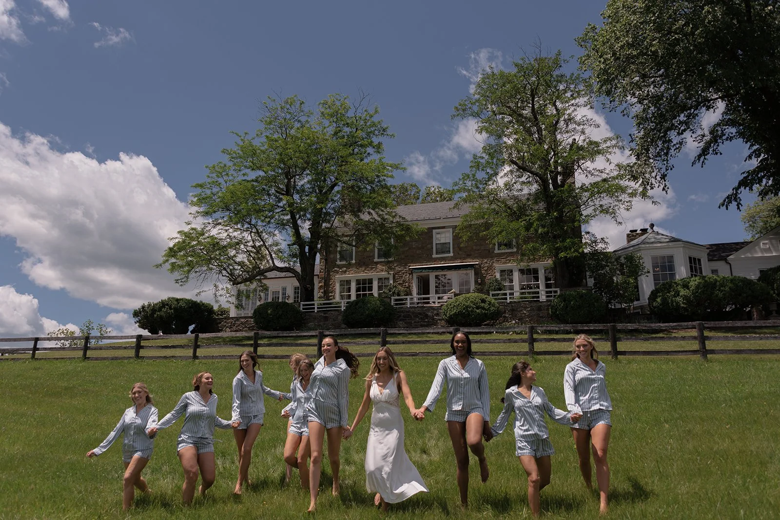 Bride and bridesmaids walking barefoot through the grassy hills behind the Manor House at Goodstone Inn on a sunny spring morning.