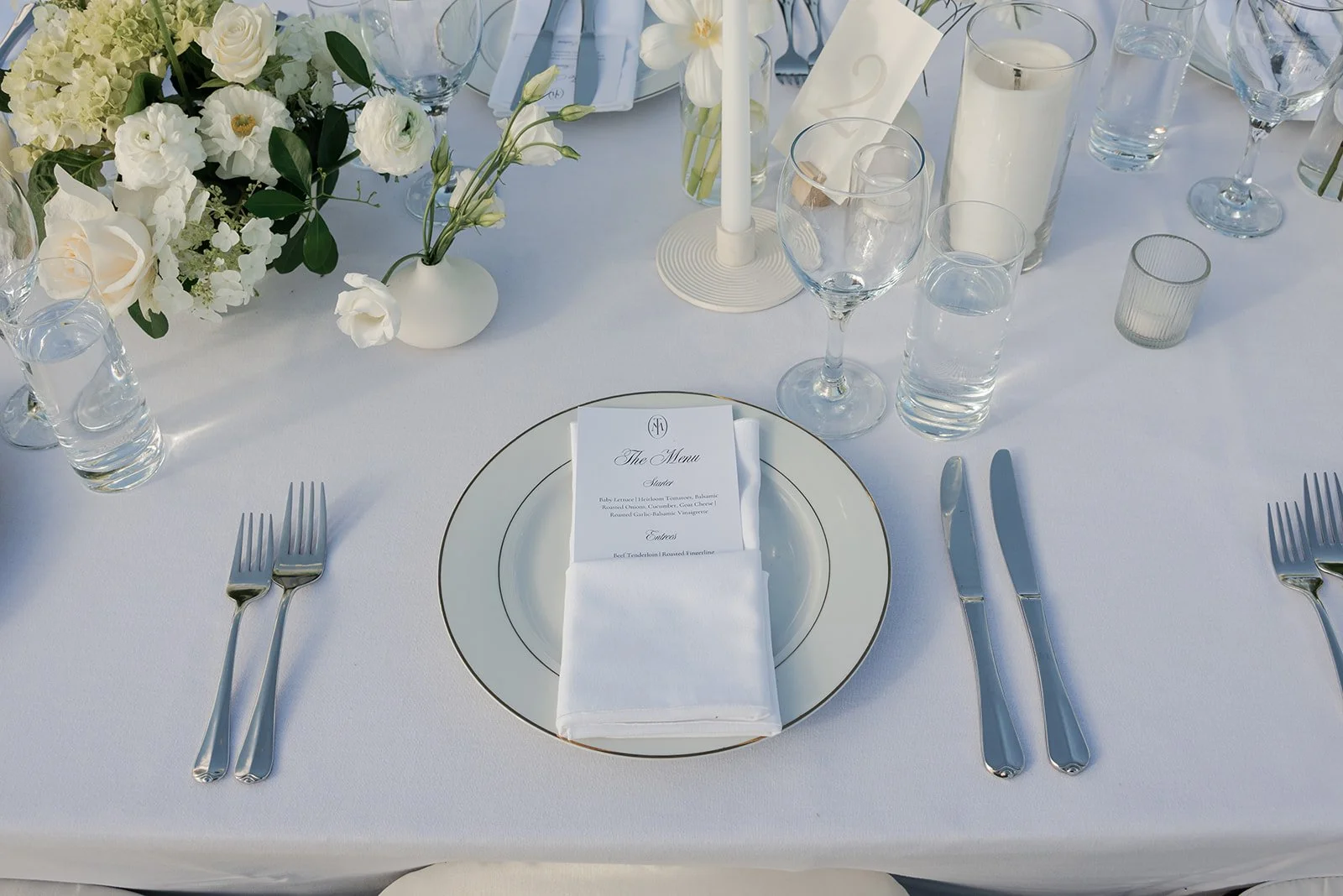 Pale green and white wedding place setting surrounded by candles and ivory flowers at Goodstone Inn.