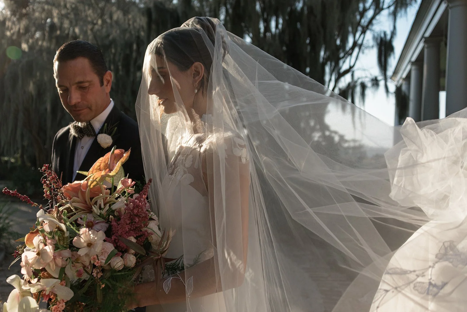 Bride wearing a flowing veil and holding a bouquet as her father takes her hand to walk her down the aisle at the River Course at Kiawah Island Resort, photographed with a fashion-inspired editorial perspective.