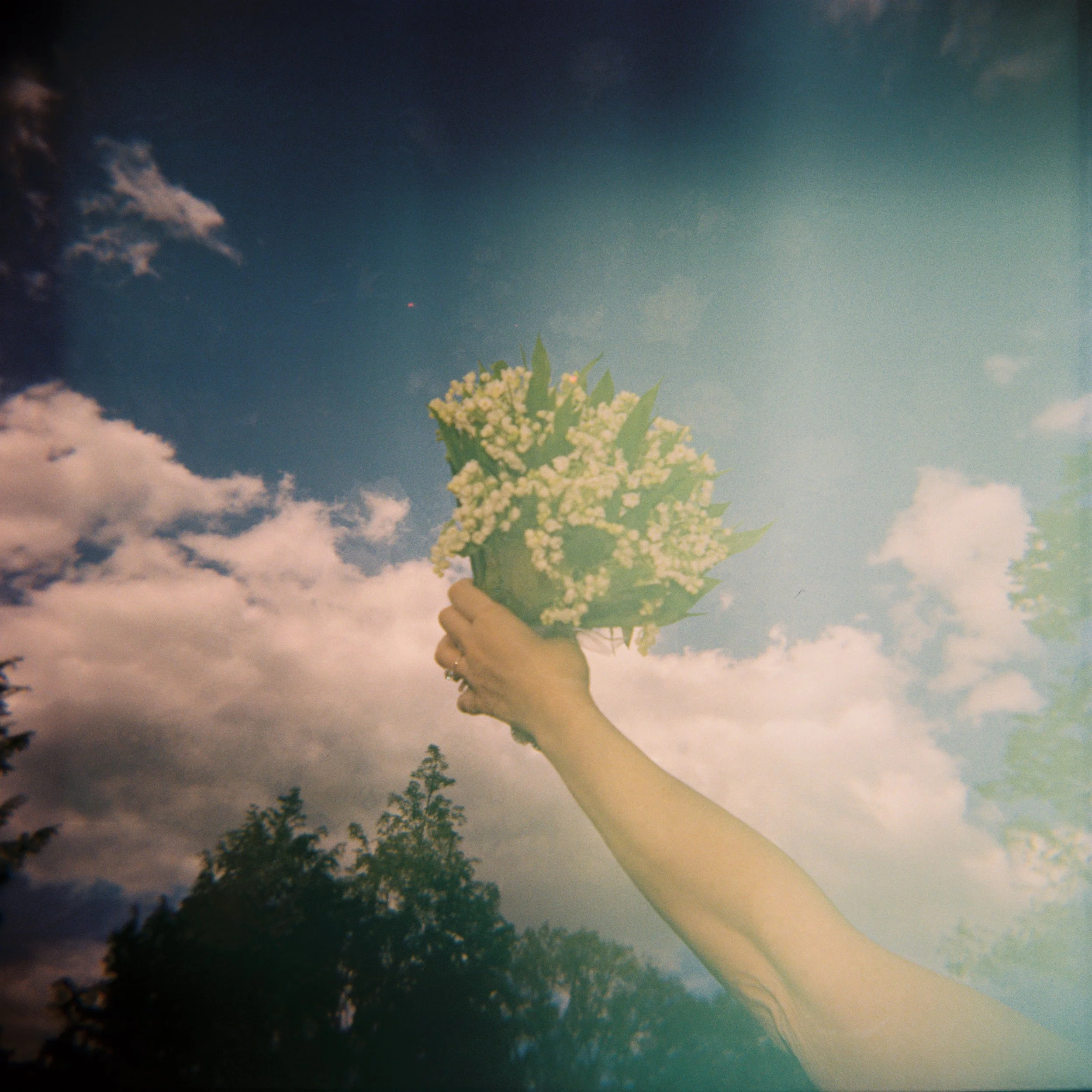 Artistic wedding photograph of a bride’s lily of the valley bouquet held against a blue sky, capturing a dreamy editorial perspective.