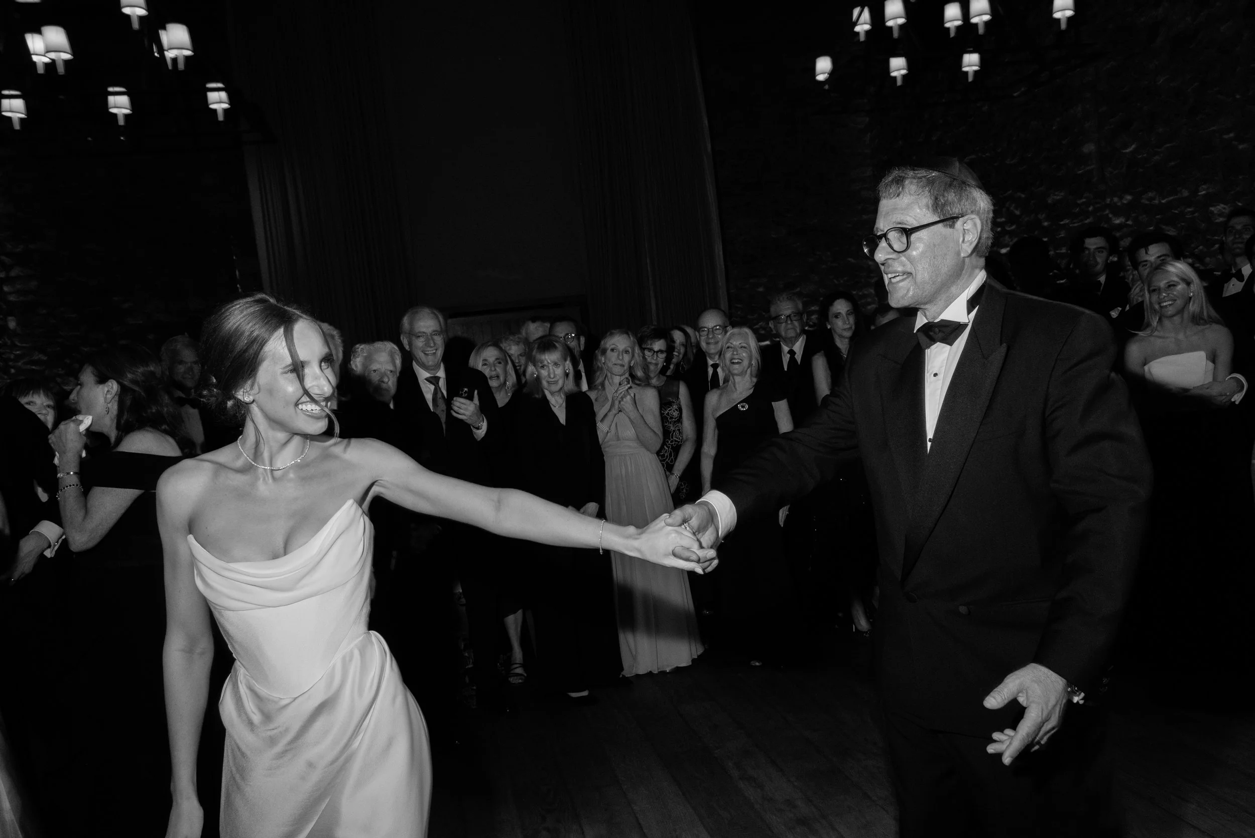 The bride shares a dance with her father surrounded by guests at the evening reception.