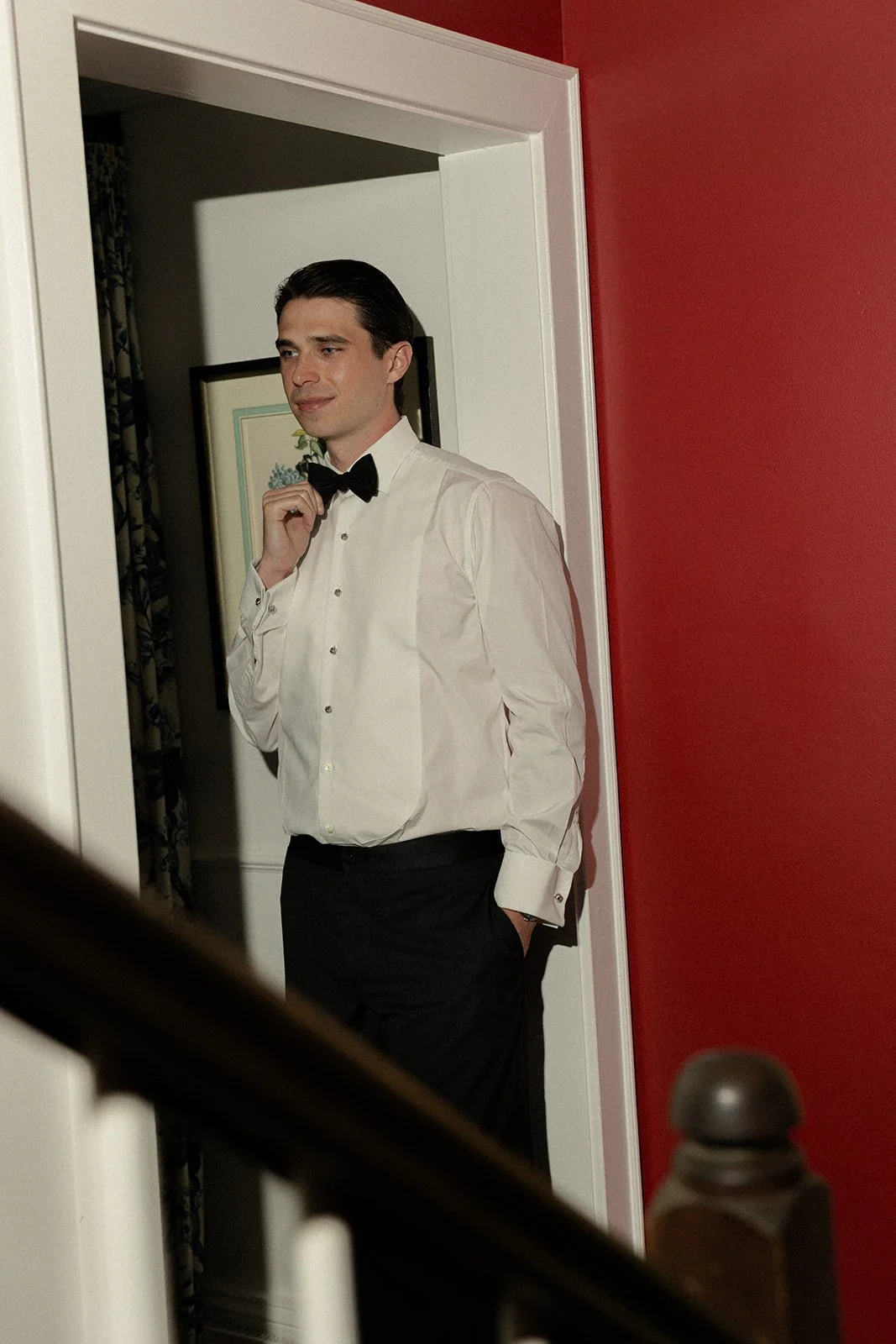 Groom in a black tuxedo photographed through a doorway while getting ready at the Spring House at Goodstone Inn.