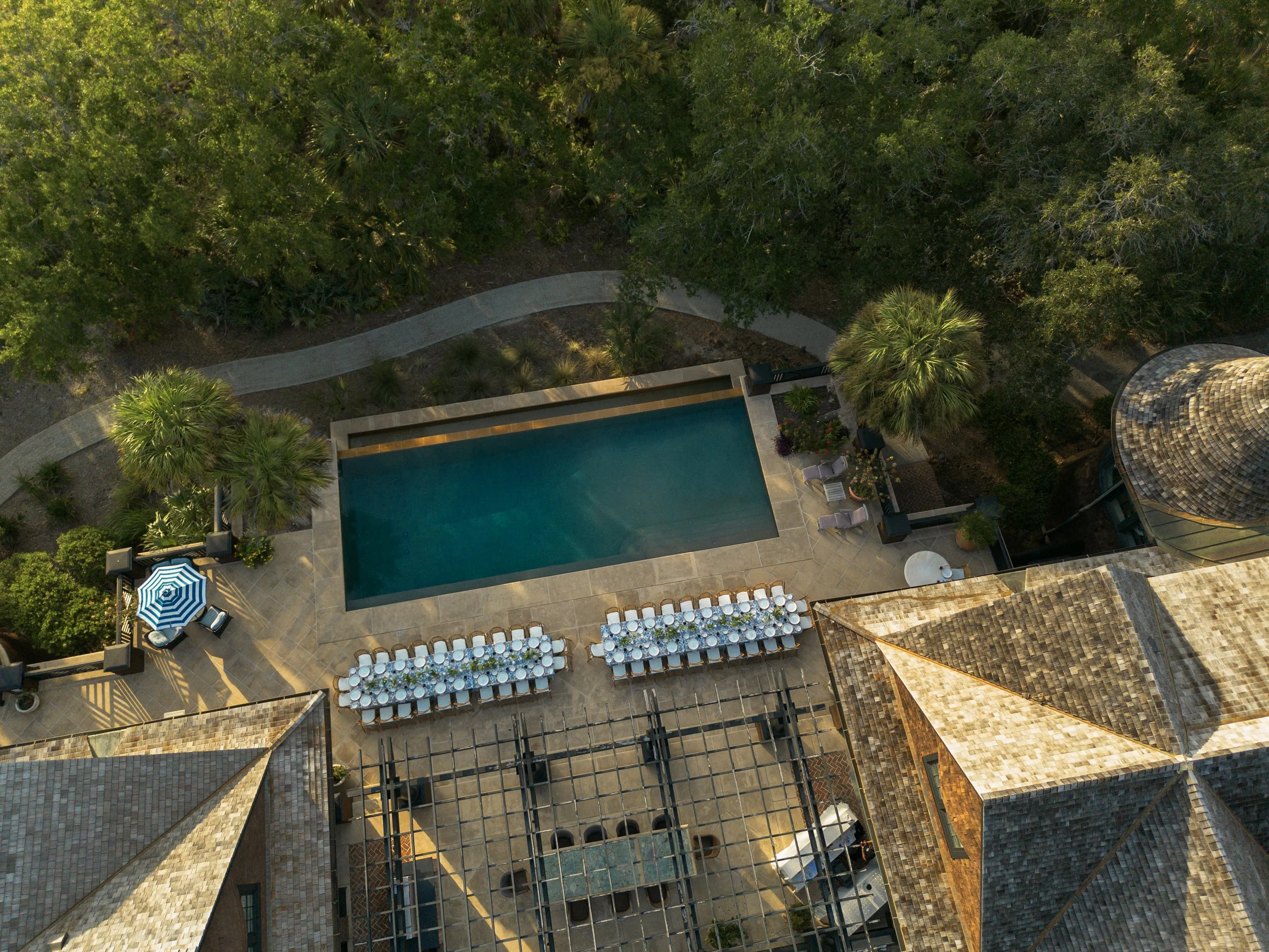 Aerial view of two long dinner tables arranged beside a swimming pool at a private estate on Kiawah Island for Katie and Trevor’s rehearsal dinner.