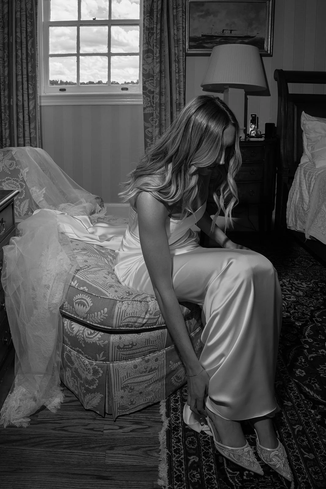 Black-and-white photograph of the bride putting on her wedding shoes.