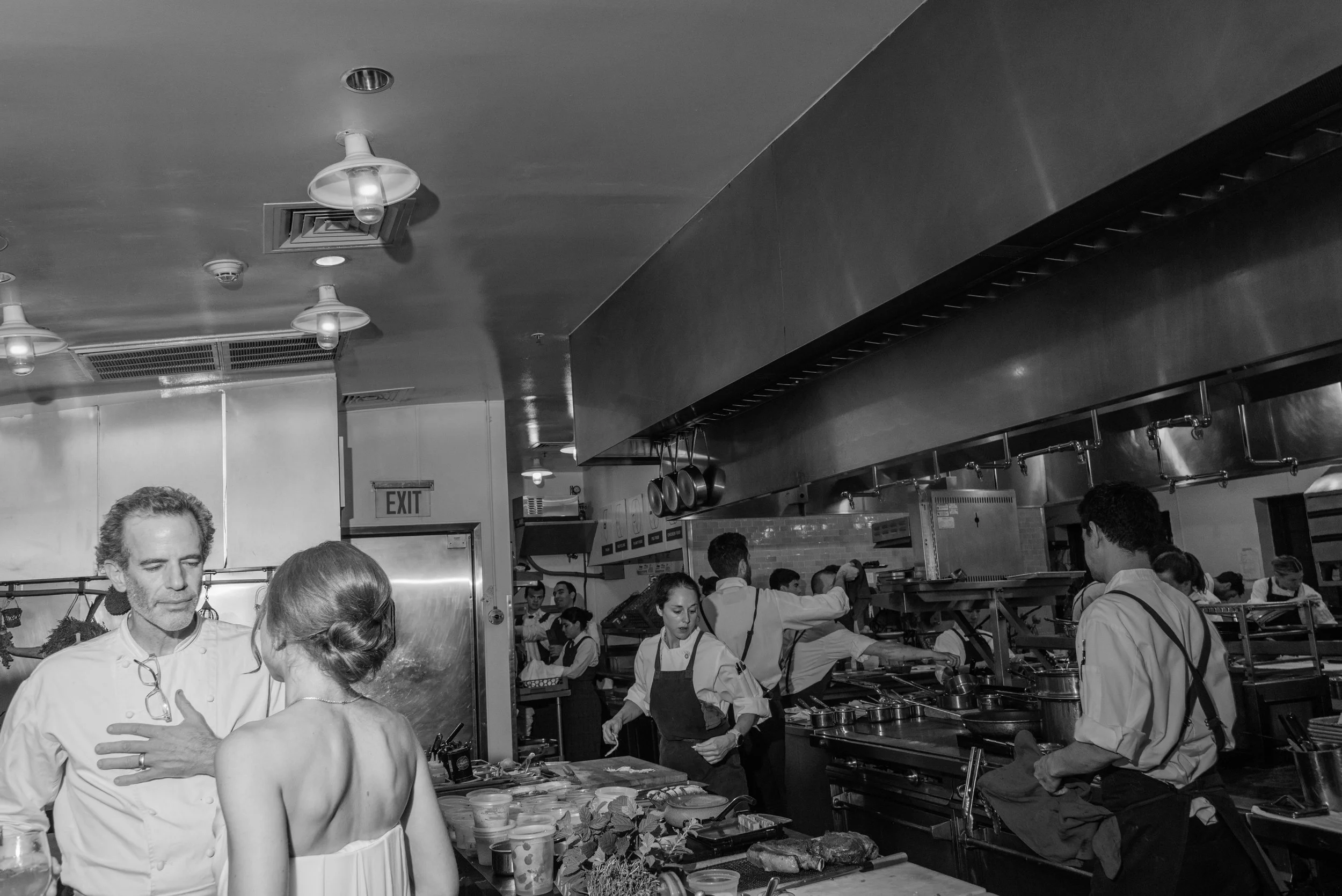 Black-and-white documentary photograph of Jennie and Will inside the Blue Hill kitchen with Chef Dan Barber during their wedding dinner.