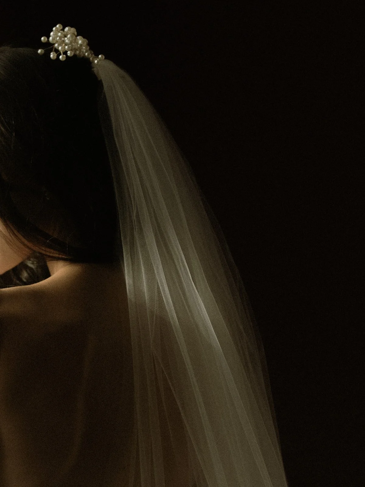 Moody, fine art close-up of a bride wearing her veil and pearl headpiece photographed against a dark background at the William Aiken House in Charleston.