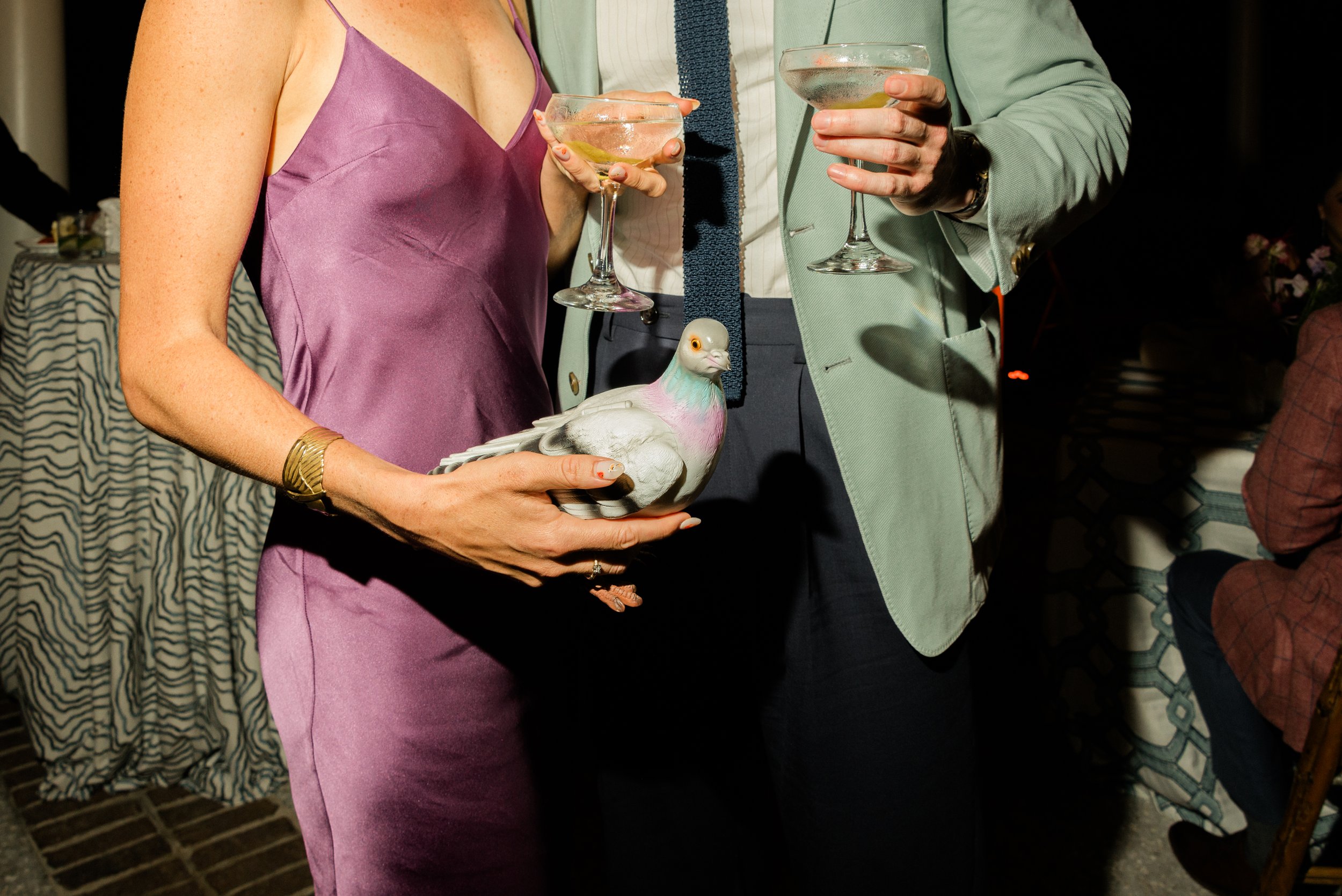 Welcome-party guest in a purple satin dress holds a pigeon purse while others raise cocktails at Turtle Point Clubhouse on Kiawah Island.