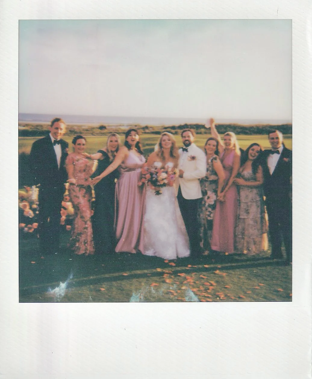 A Polaroid of Katie, Trevor, and their wedding party beneath the open sky at The Ocean Course on Kiawah Island.
