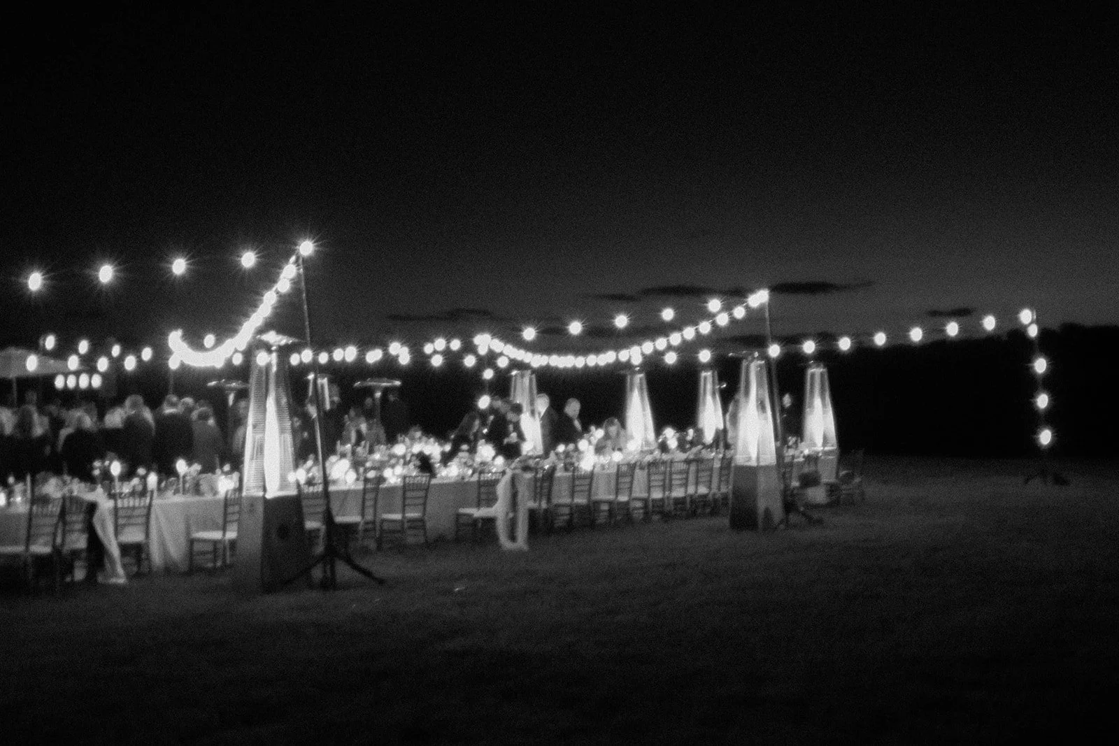 Black-and-white wide view of the outdoor Goodstone Inn reception glowing beneath string lights at night.