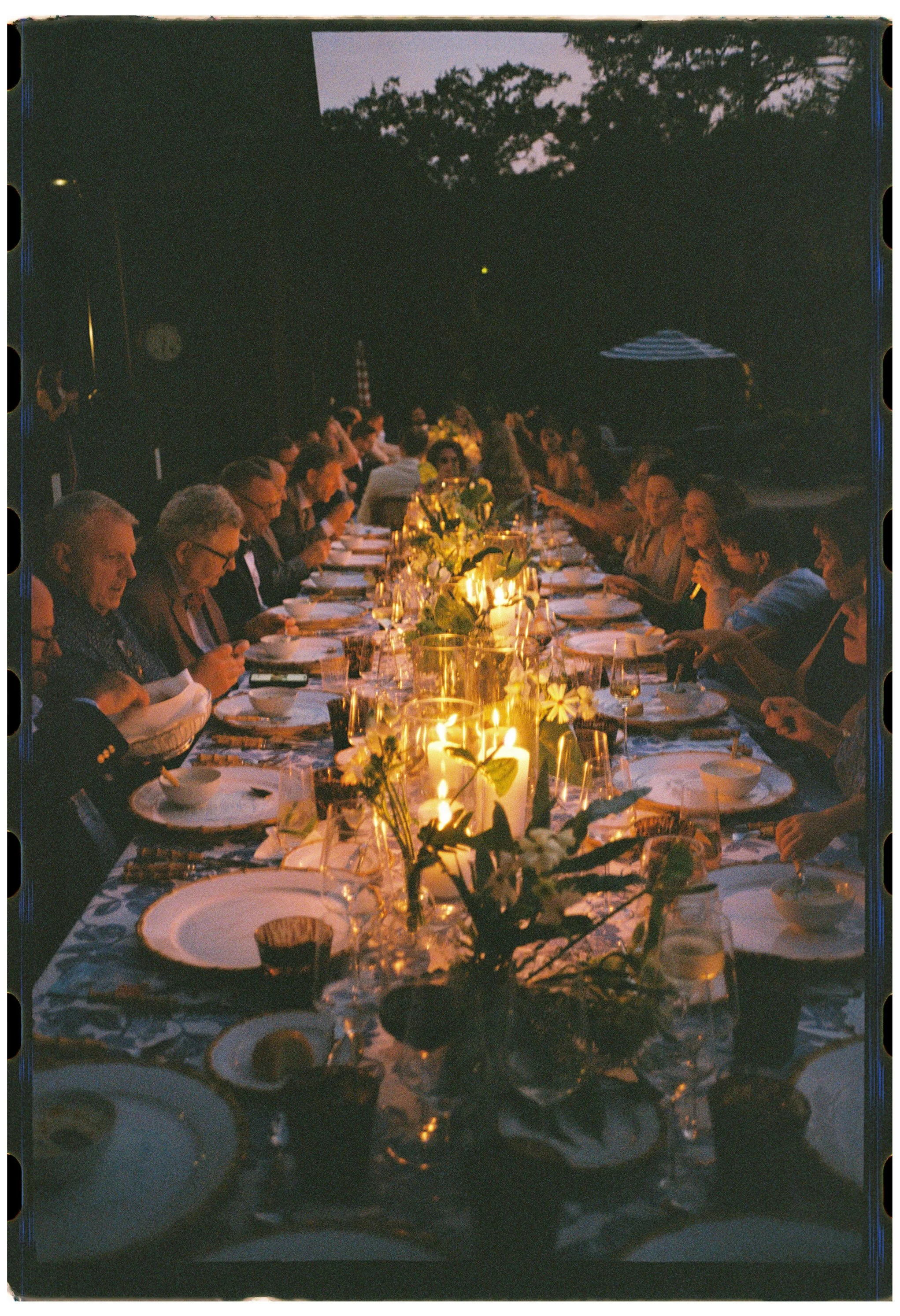 Guests dine around a long candlelit table after sunset during Katie and Trevor’s intimate rehearsal dinner on Kiawah Island.