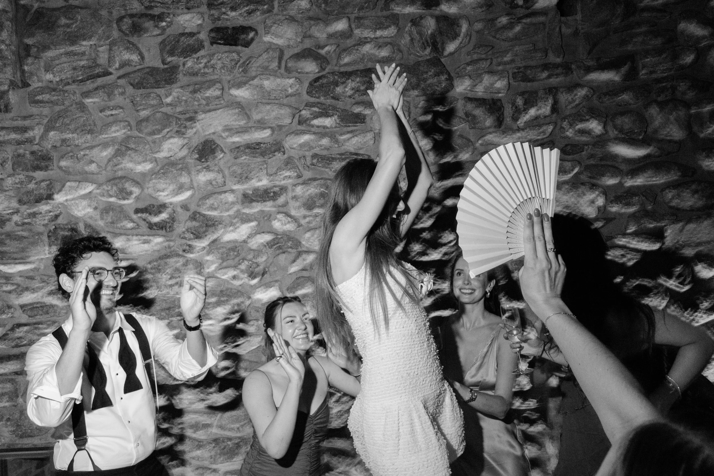 Black-and-white photograph of Jennie dancing with friends on the dining tables during the lively wedding reception.