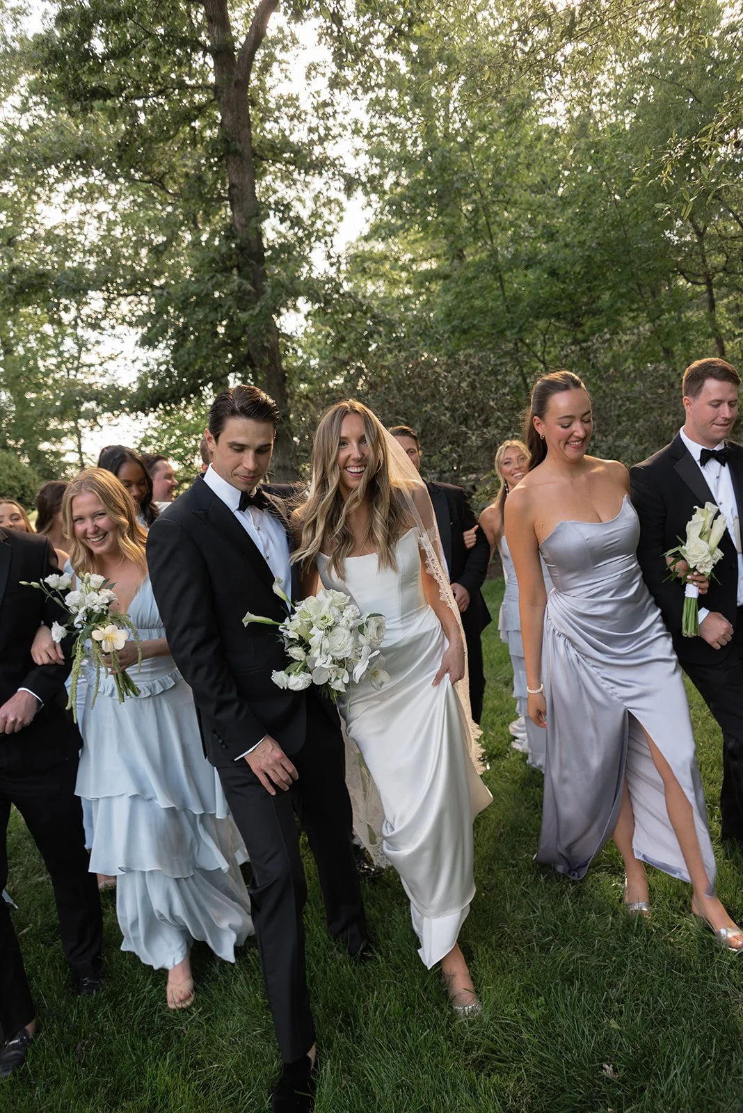 Wedding party in shades of blue and formal tuxes walking together through the gardens at Goodstone Inn.