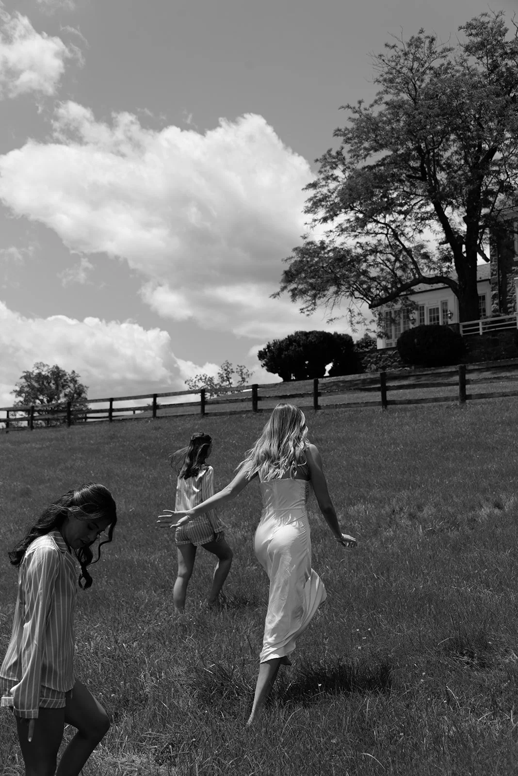 Black-and-white photograph of the bride and bridesmaids walking through the open fields at Goodstone Inn.