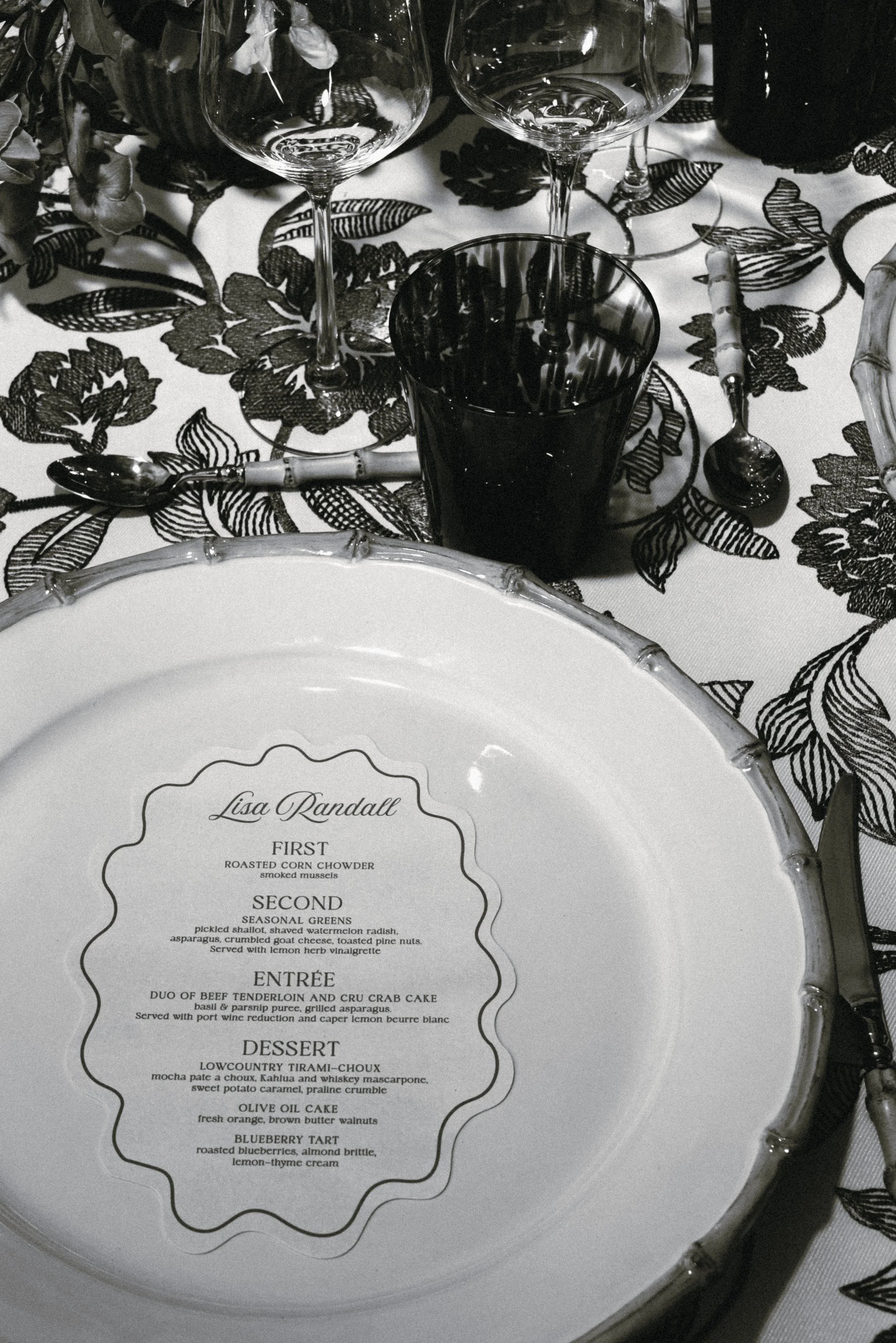 Illustrated rehearsal-dinner menu displayed on a scalloped plate with botanical black-and-white linens at a private estate on Kiawah Island.