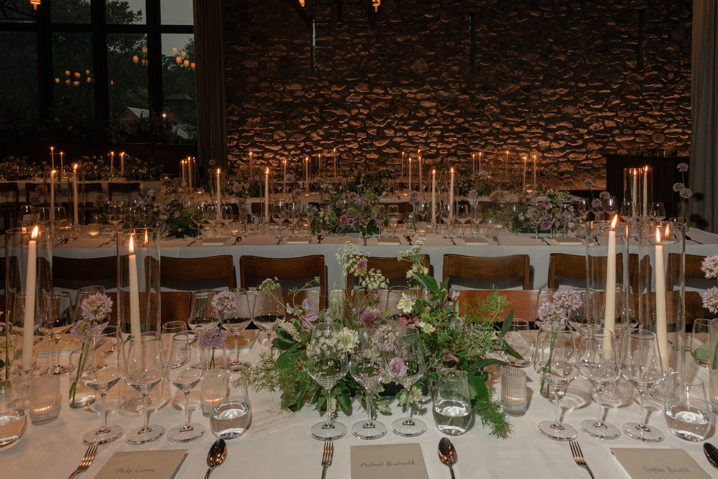Three long dinner tables layered with seasonal florals provided by Wild and Birch, glassware and candlelight for Jennie and Will’s reception.