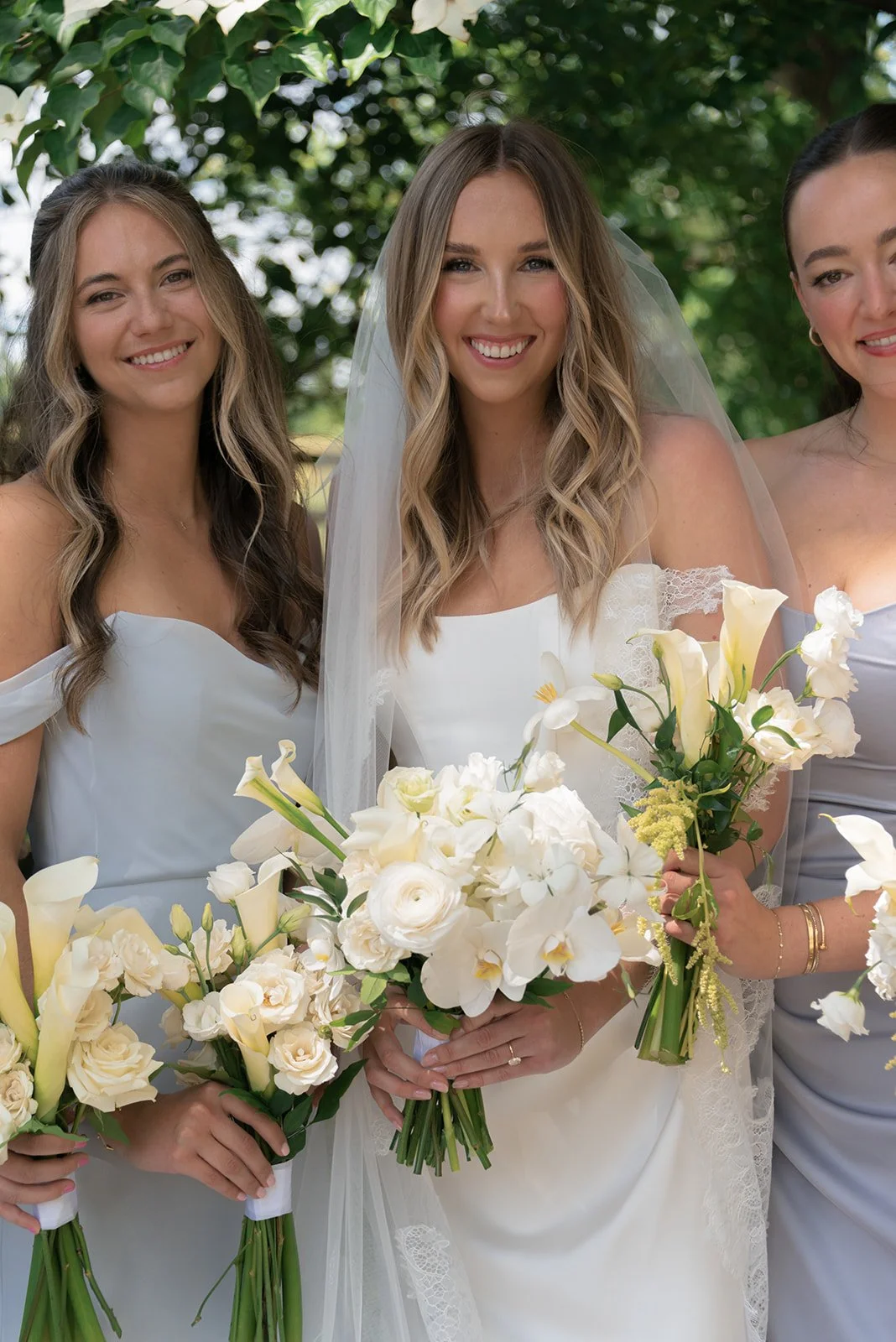Bride and bridesmaids holding white bouquets by Steelcut Flower Co. while gathered together outdoors at Goodstone Inn.