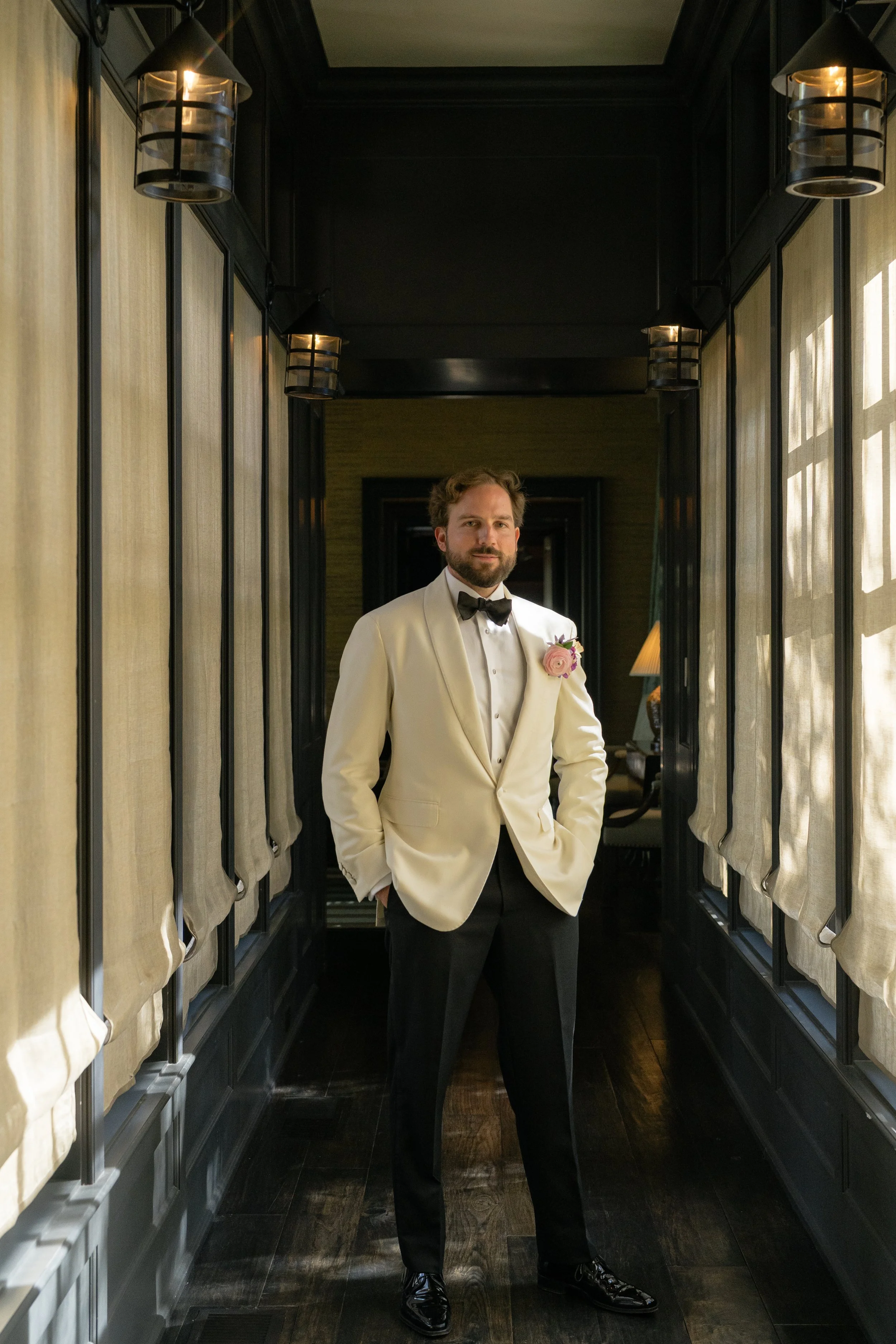 Trevor stands in a shadowed corridor wearing a white dinner jacket and black bow tie before the Kiawah Island ceremony.