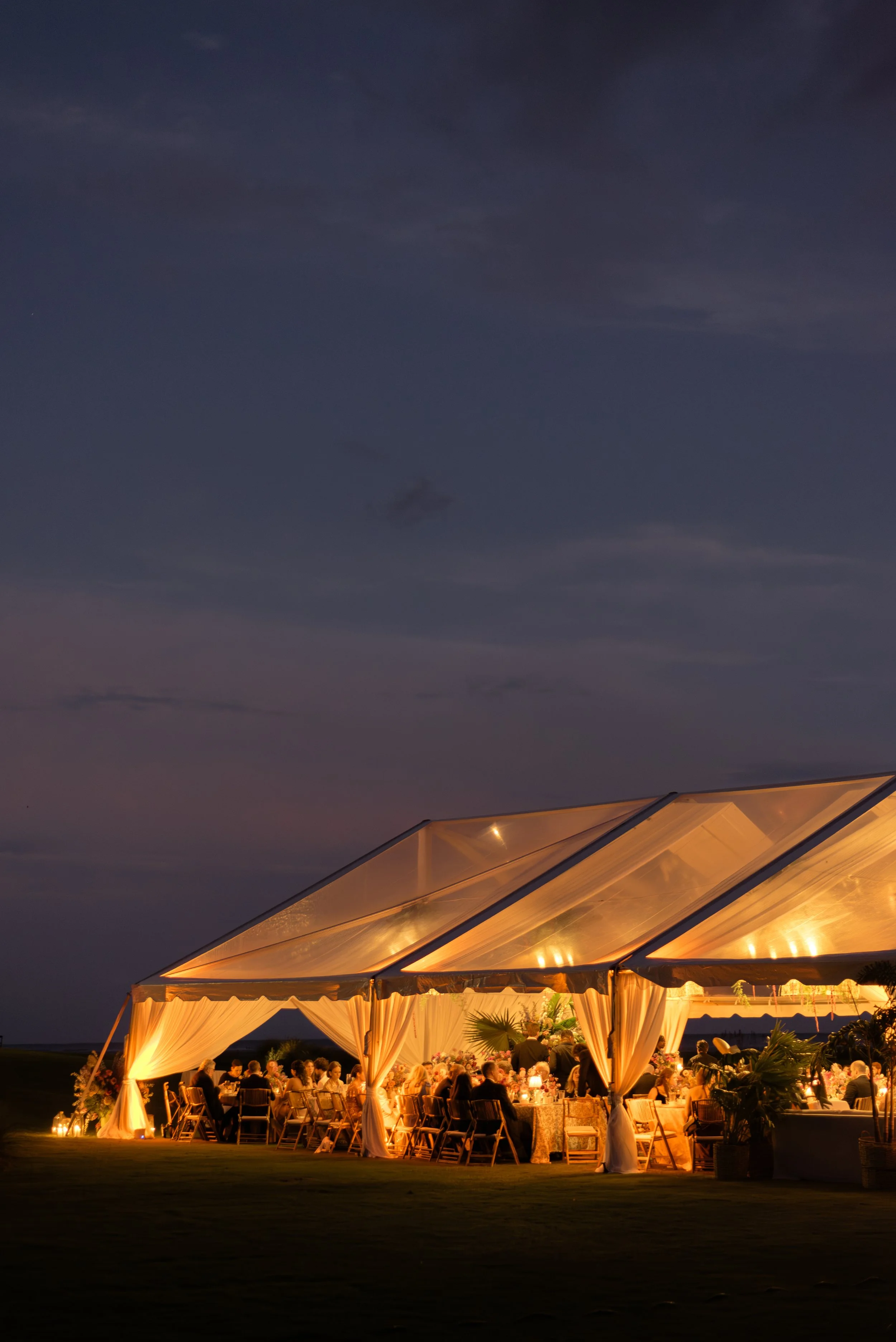 Aerial-inspired evening photograph of a beautifully lit wedding tent reception overlooking the landscape at the Ocean Course at Kiawah Island Resort in South Carolina. 