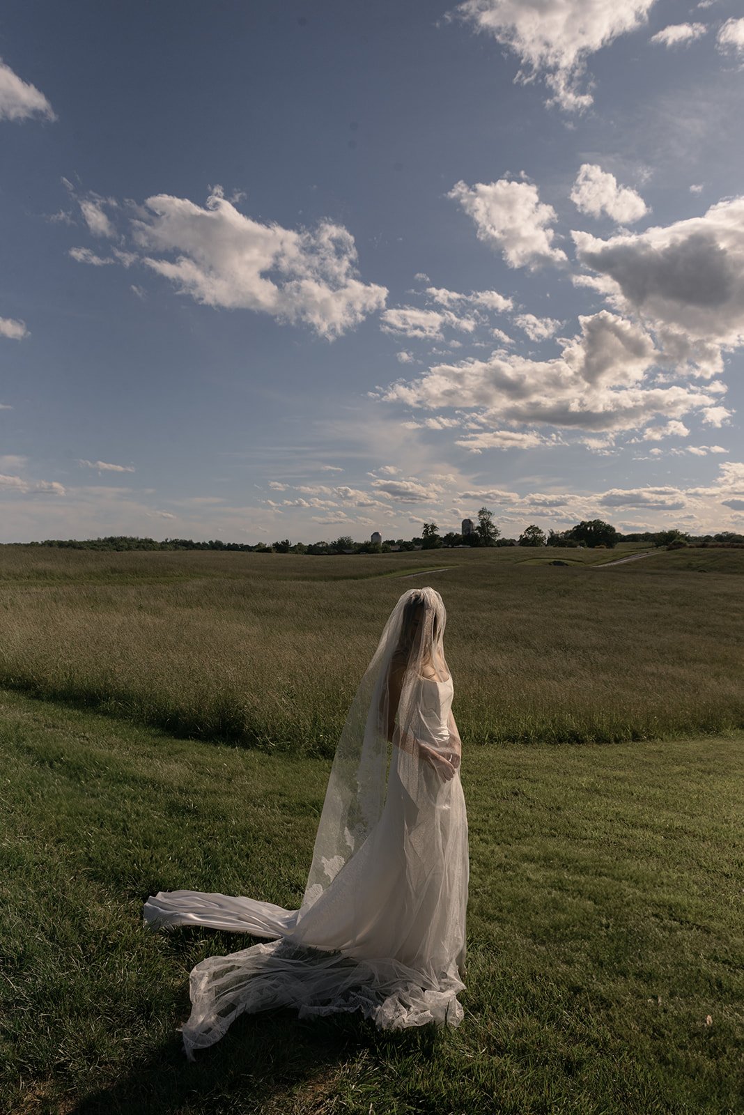 Bride walking alone through the Hayfield at Goodstone Inn with her cathedral veil draped over her.