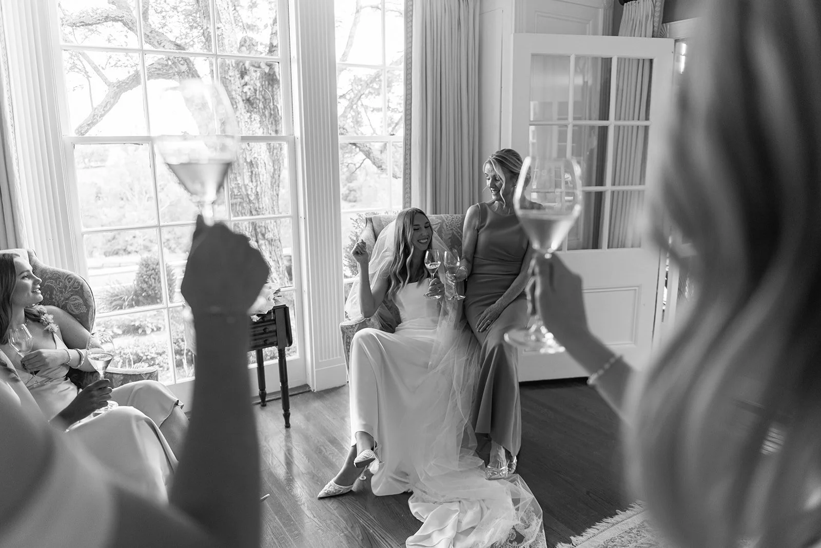 Black-and-white candid of the bride surrounded by bridesmaids sharing a glass of rosé inside the Manor House at Goodstone Inn.