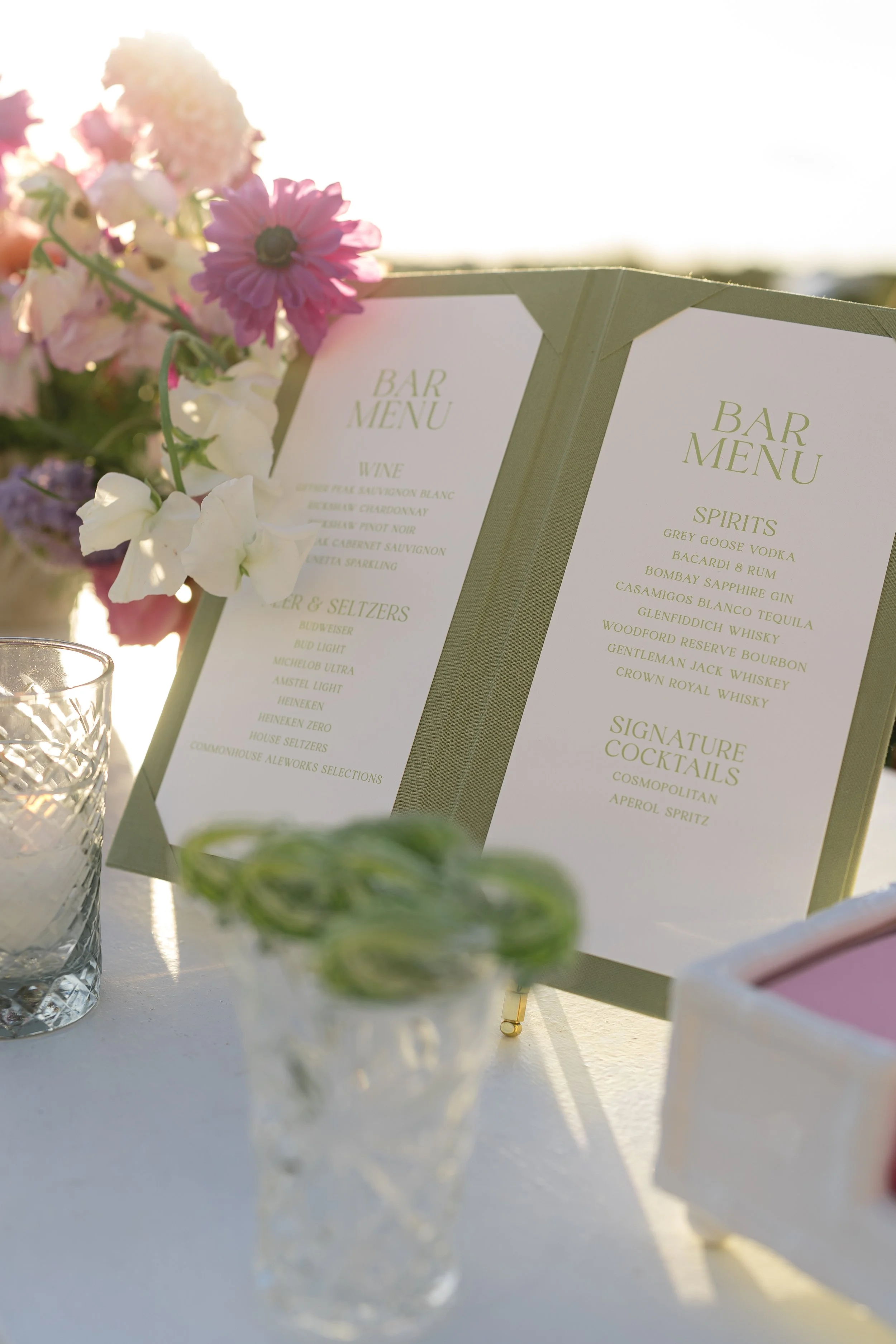 Green cocktail menus decorated with pink flowers stand on the outdoor bar during the Kiawah Island wedding cocktail hour.