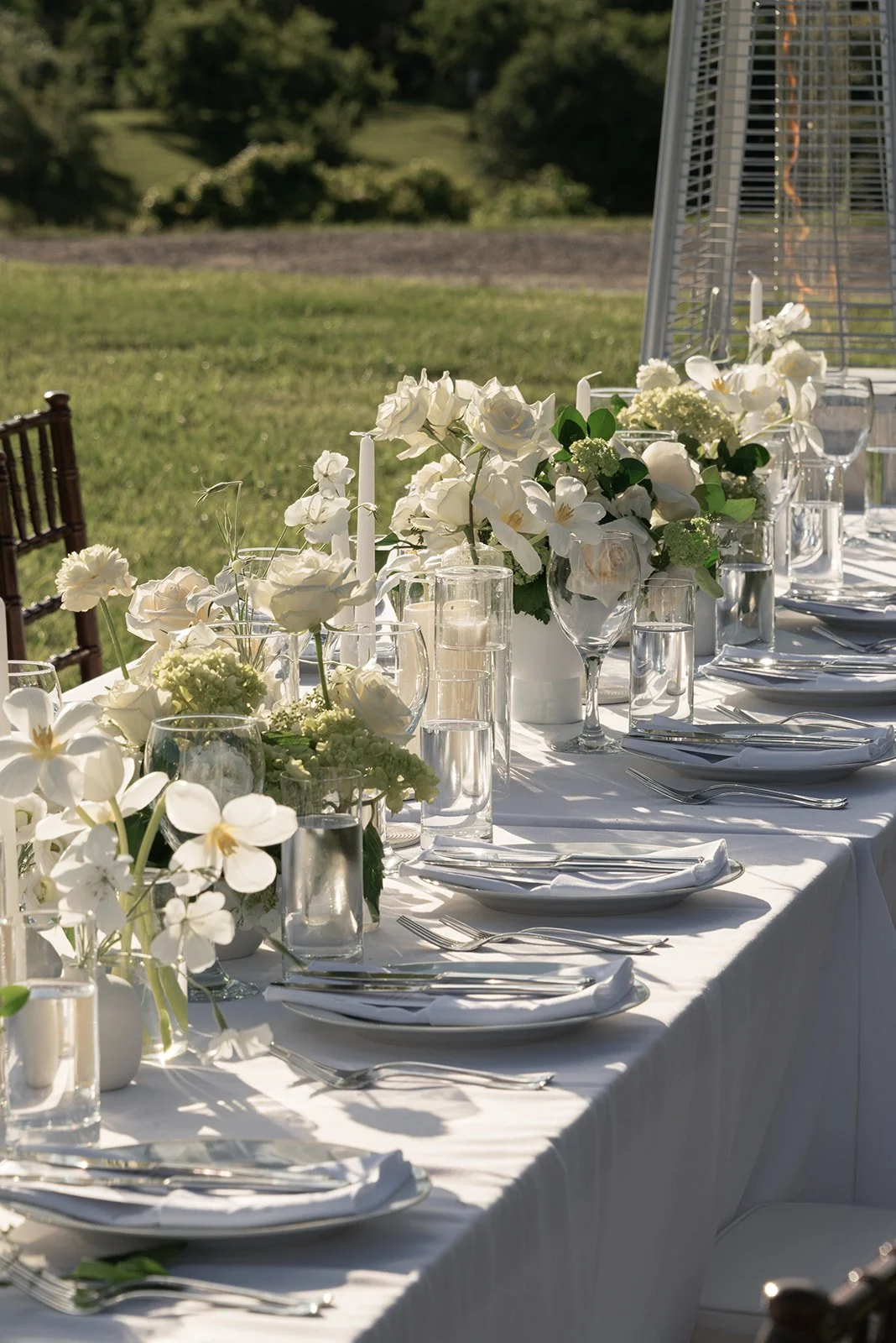 Long white dinner table styled with candles and ivory flowers for an outdoor reception at Goodstone Inn.