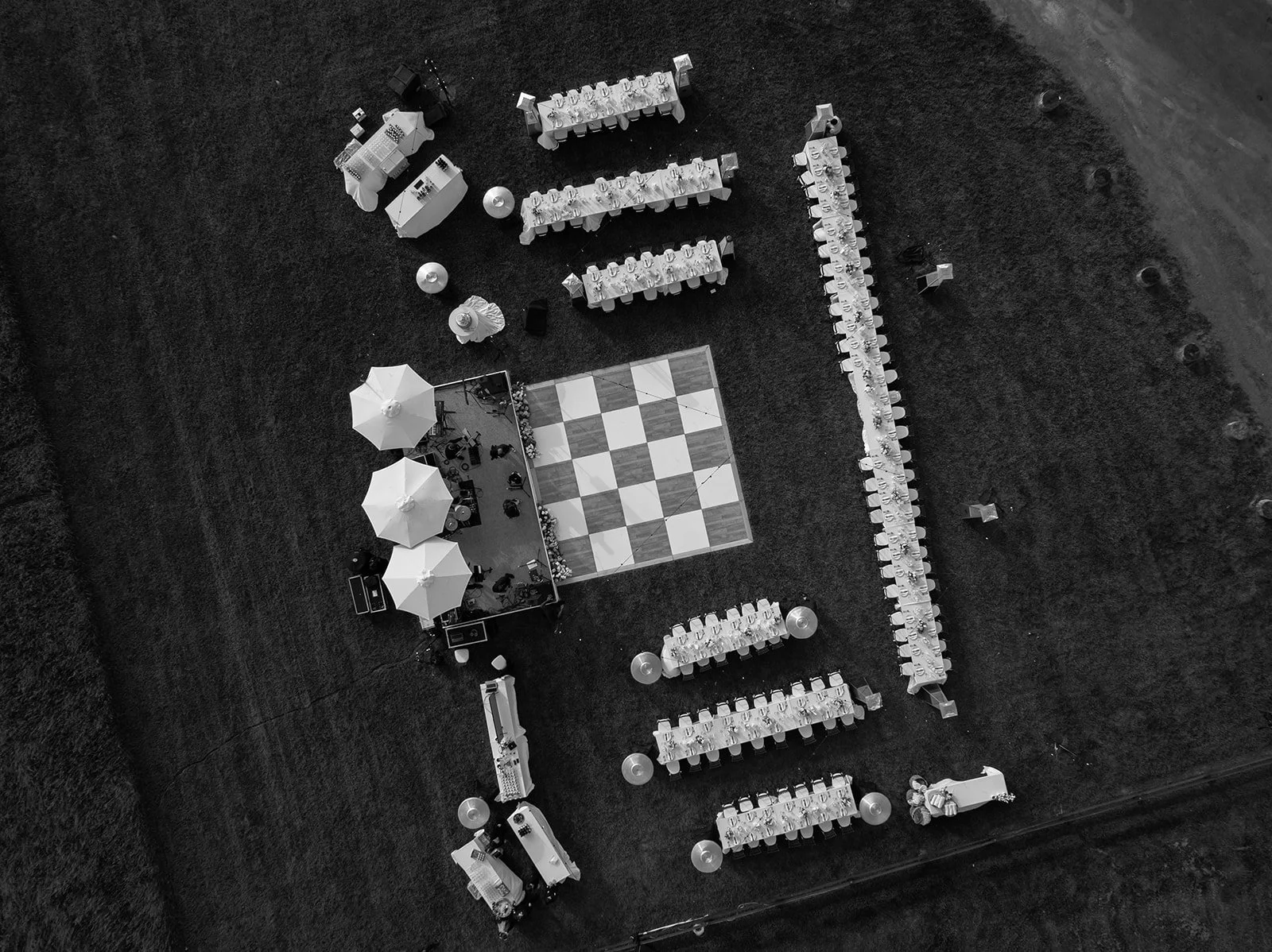 Black-and-white aerial drone view of long dinner tables and a checkerboard dance floor in the Hayfield at Goodstone Inn.