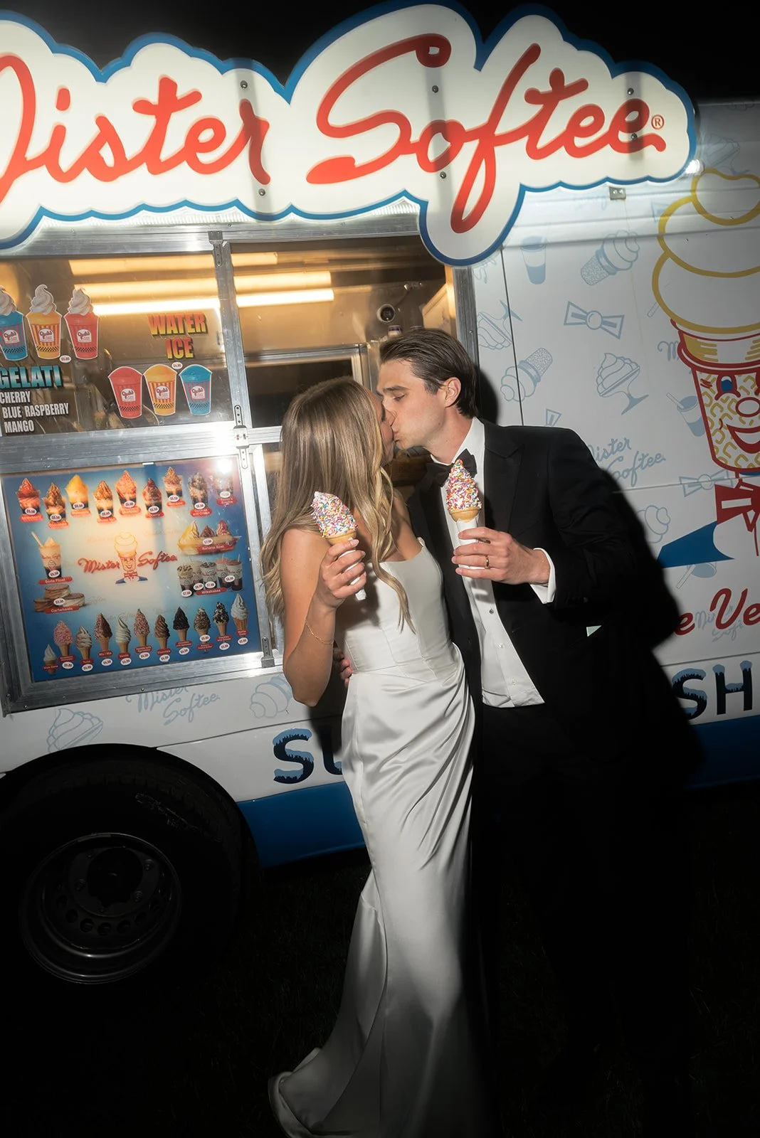 Bride and groom kissing while holding sprinkle-covered ice cream cones beside a Mister Softee truck at their Goodstone Inn wedding.