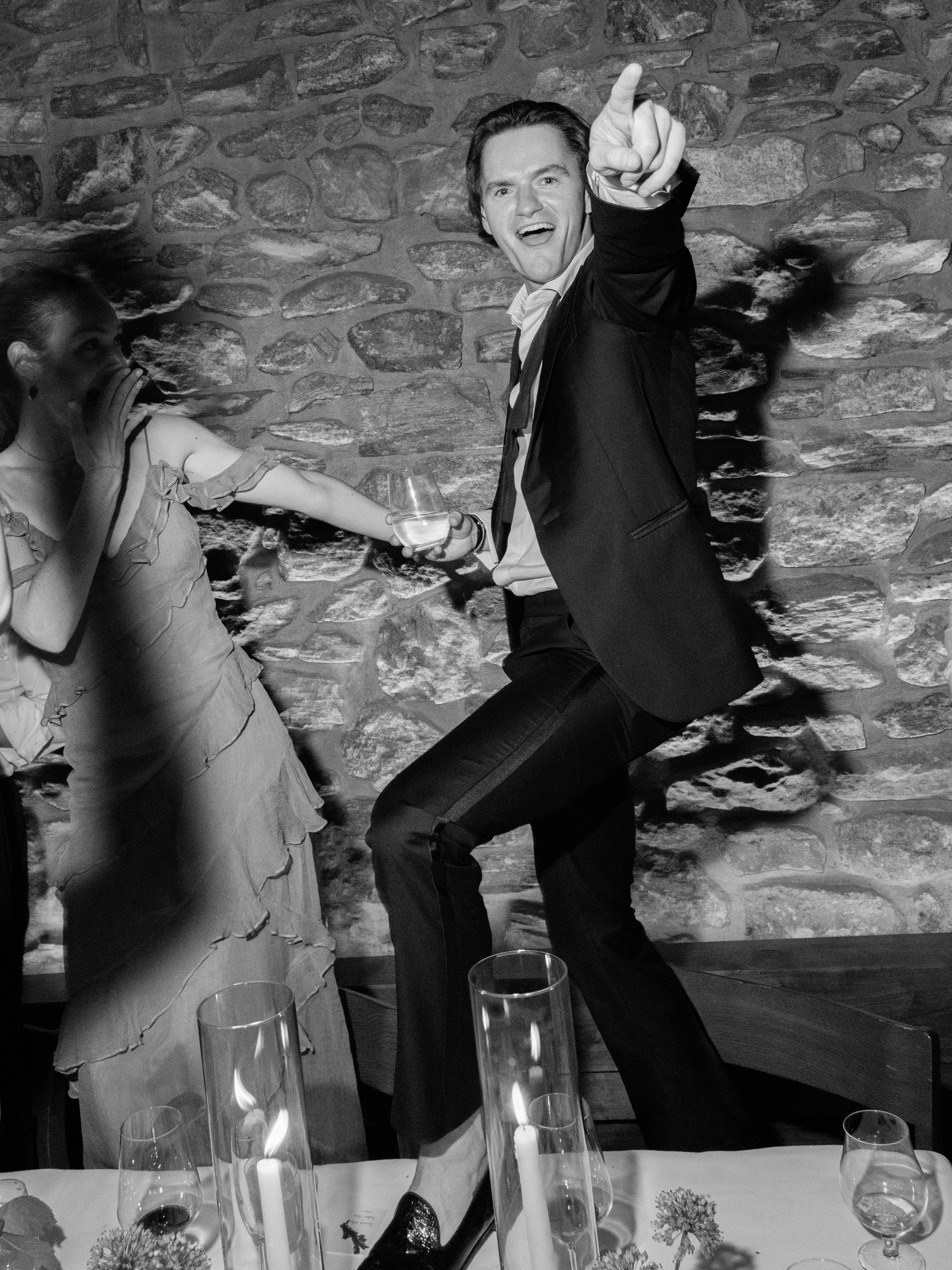 Black-and-white candid of a guest dancing on the dining table during the energetic late-night reception.