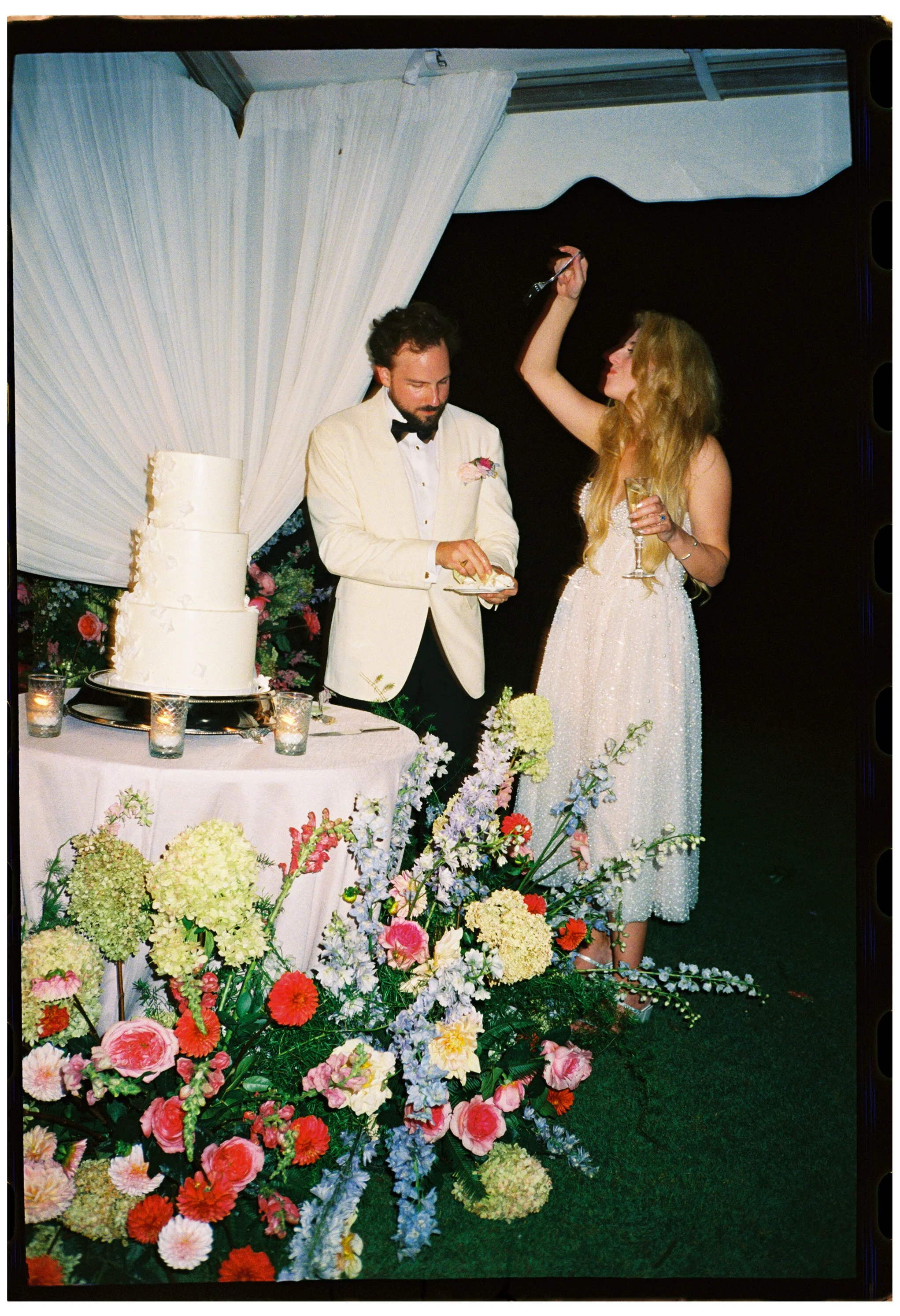 The bride and groom cut their wedding cake beside a colorful ground-level floral installation by Festoon.