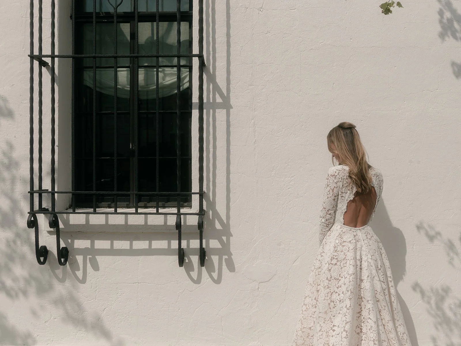 Bride standing in directional sunlight wearing an open-back lace wedding gown at Commonhouse.