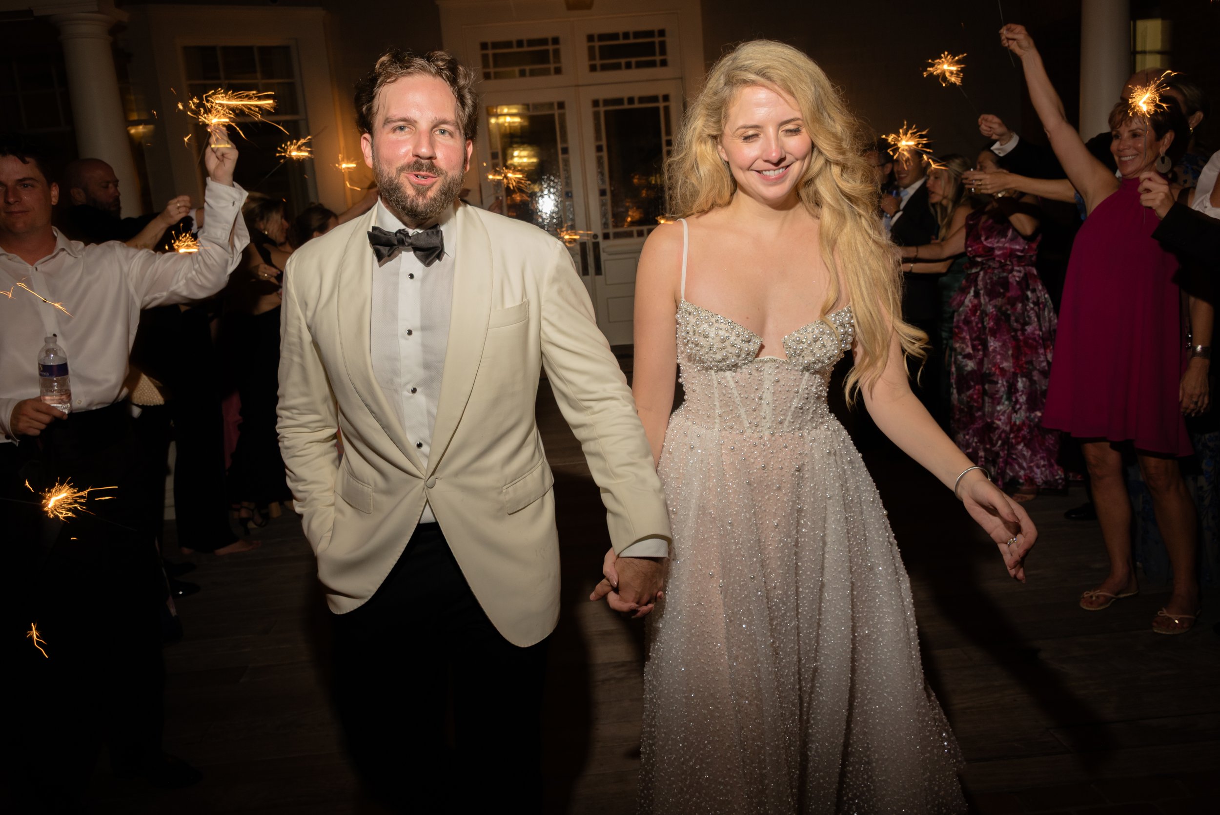 Katie and Trevor walk hand in hand through cheering guests holding sparklers after their Ocean Course reception.