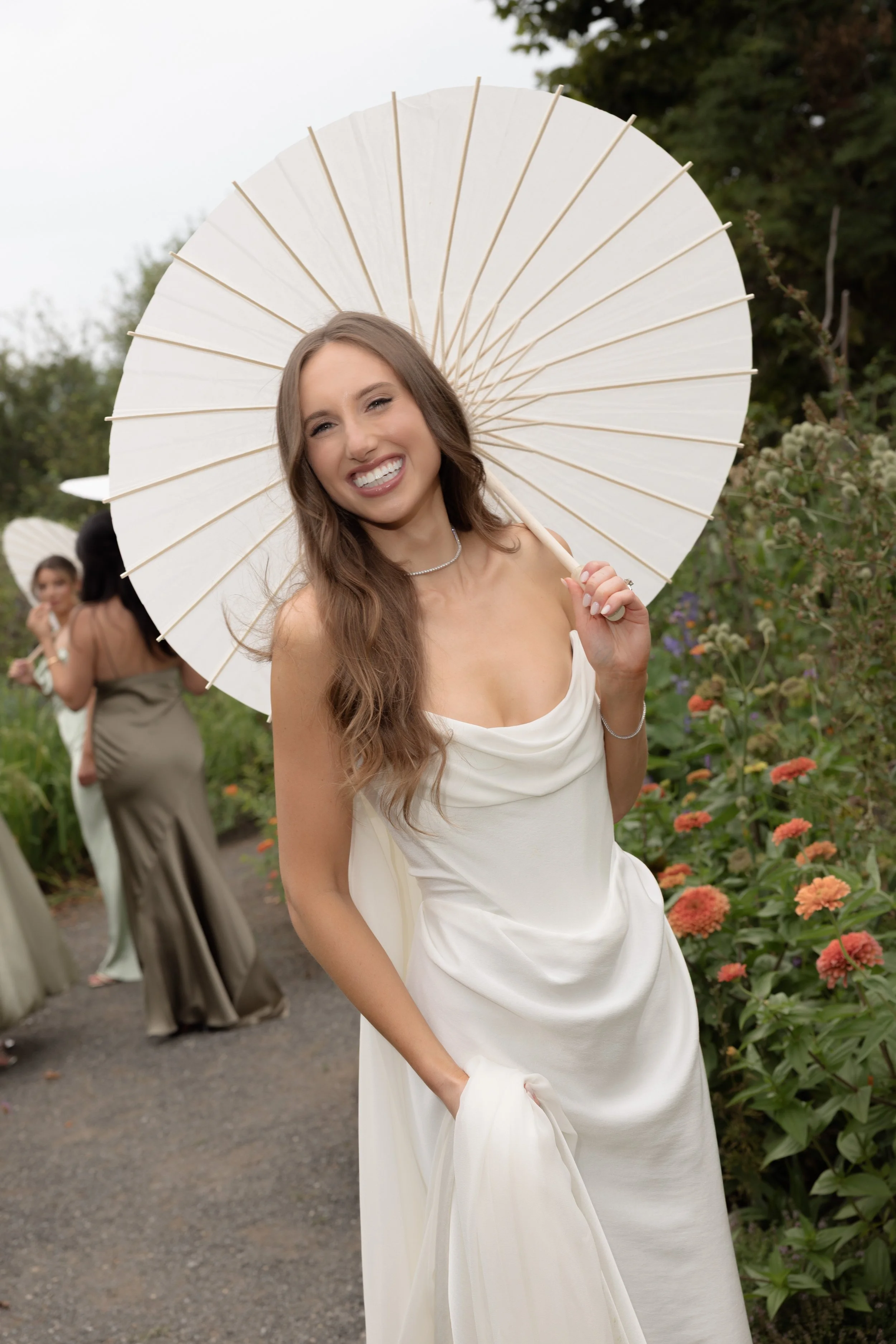 Jennie smiles beneath a white parasol while taking portraits with her bridesmaids in the gardens at Blue Hill at Stone Barns.