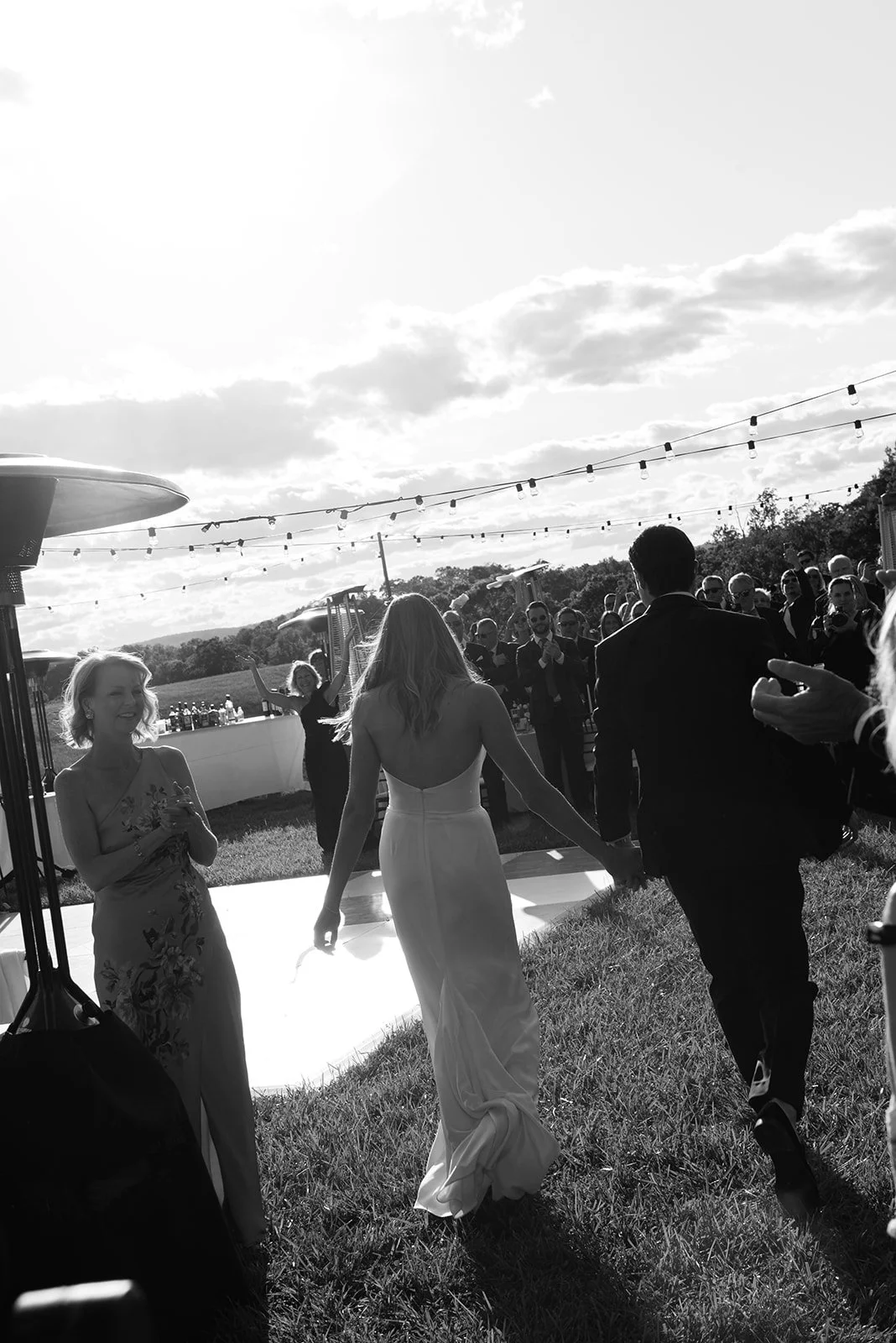 Black-and-white candid of the bride and groom walking through the Hayfield reception at Goodstone Inn.