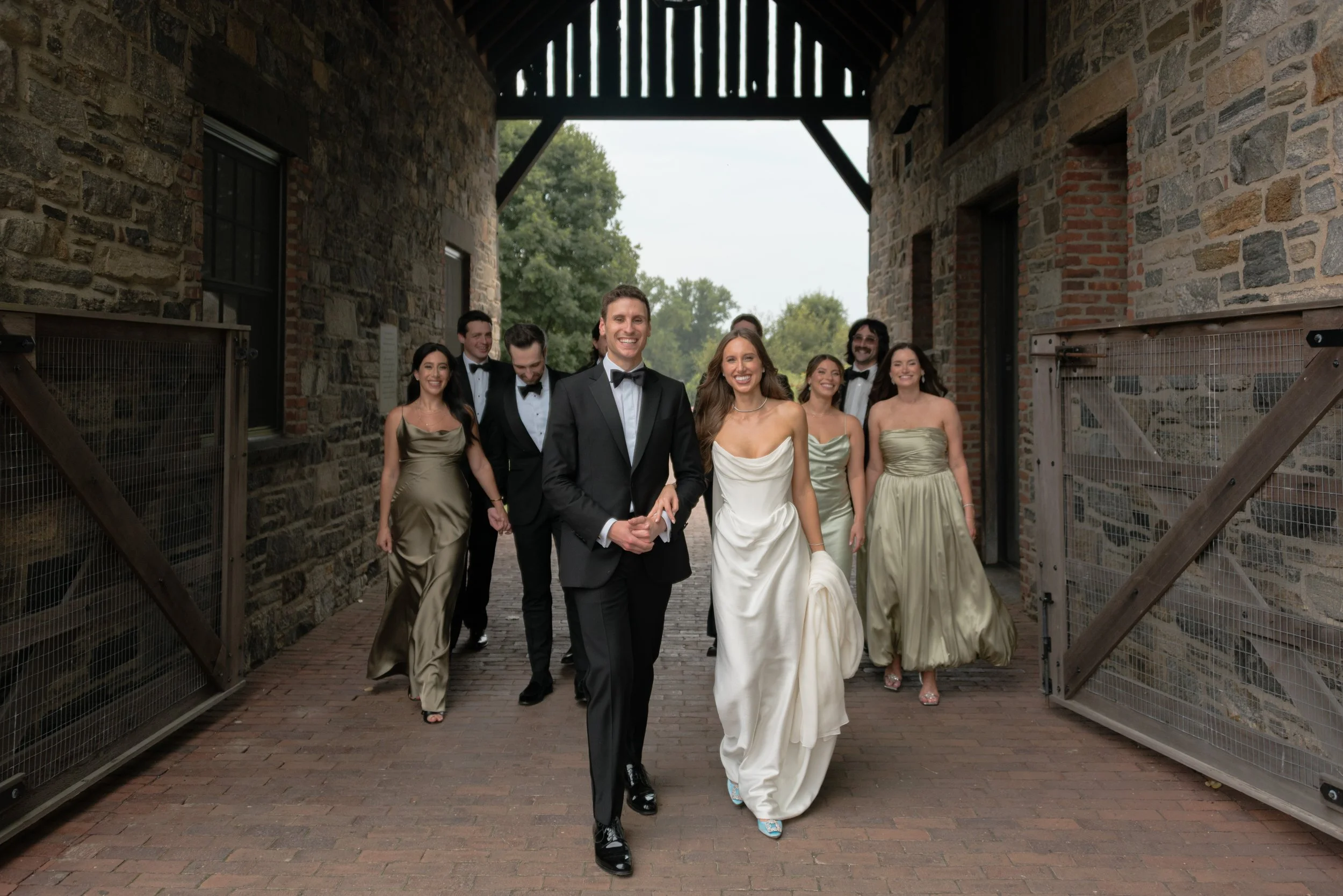 Jennie, Will and their wedding party walk together beneath the stone breezeway at Blue Hill at Stone Barns.