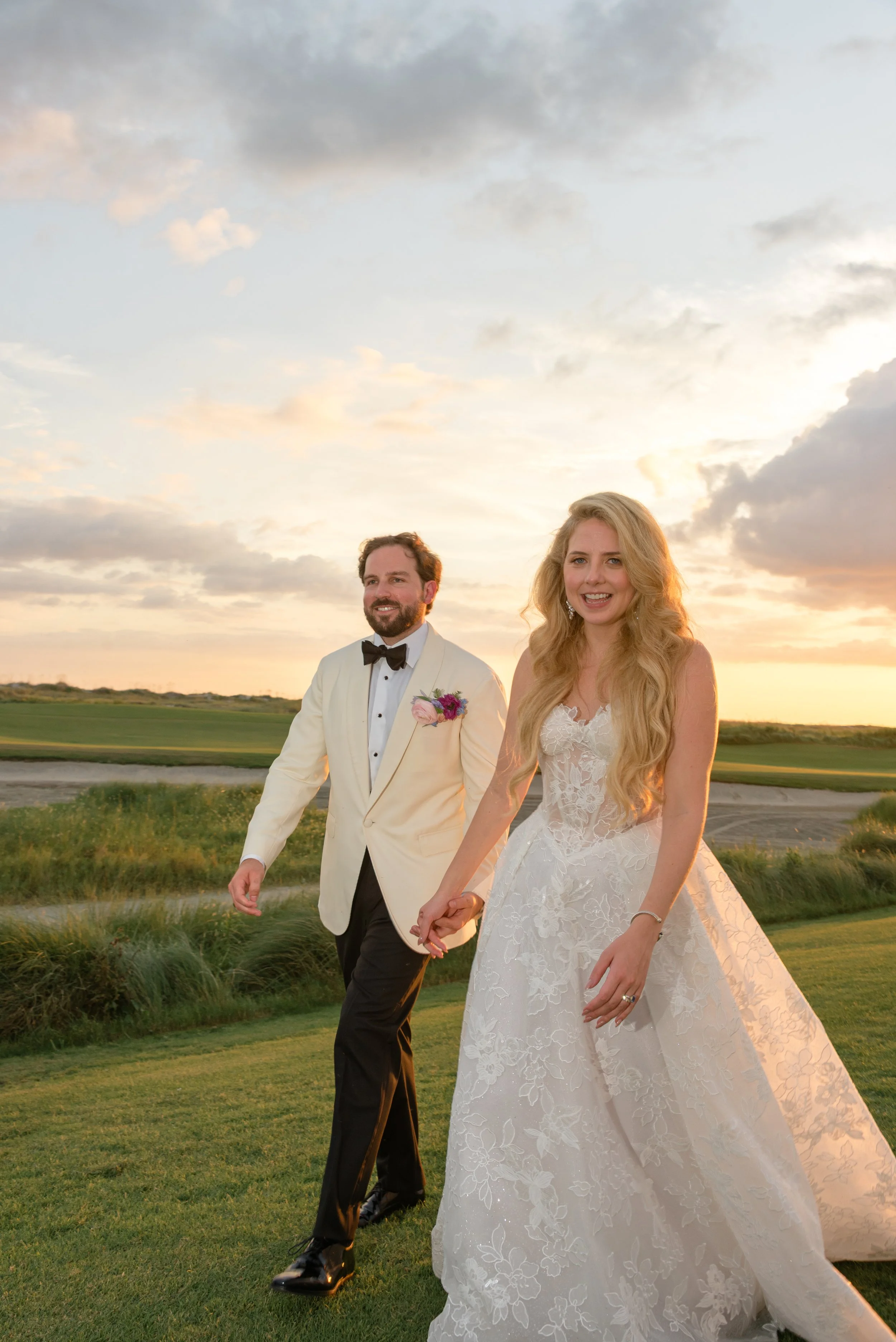The bride and groom hold hands beneath the golden evening sky before entering their Kiawah Island wedding reception.