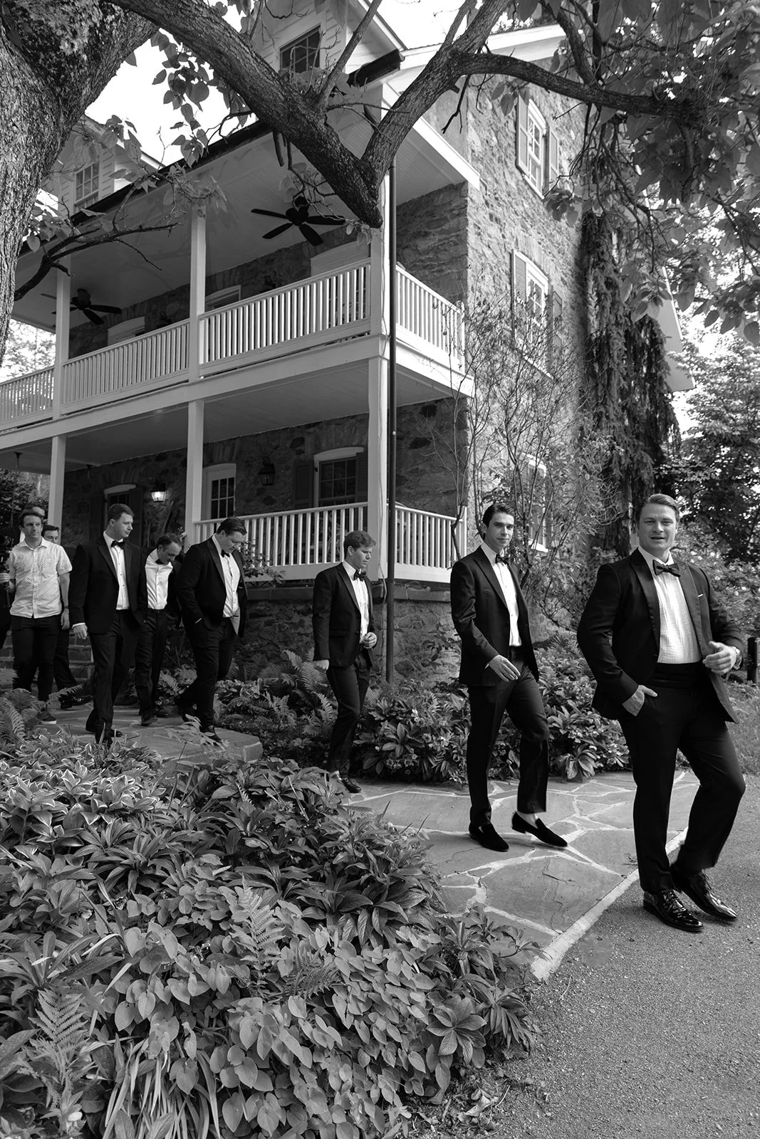 Black-and-white candid of groomsmen walking outdoors through the grounds at Goodstone Inn.