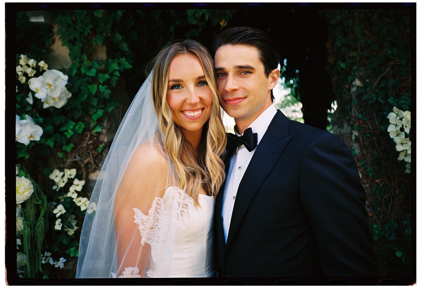 Close film portrait of the smiling bride and groom surrounded by greenery and white flowers at Goodstone Inn.