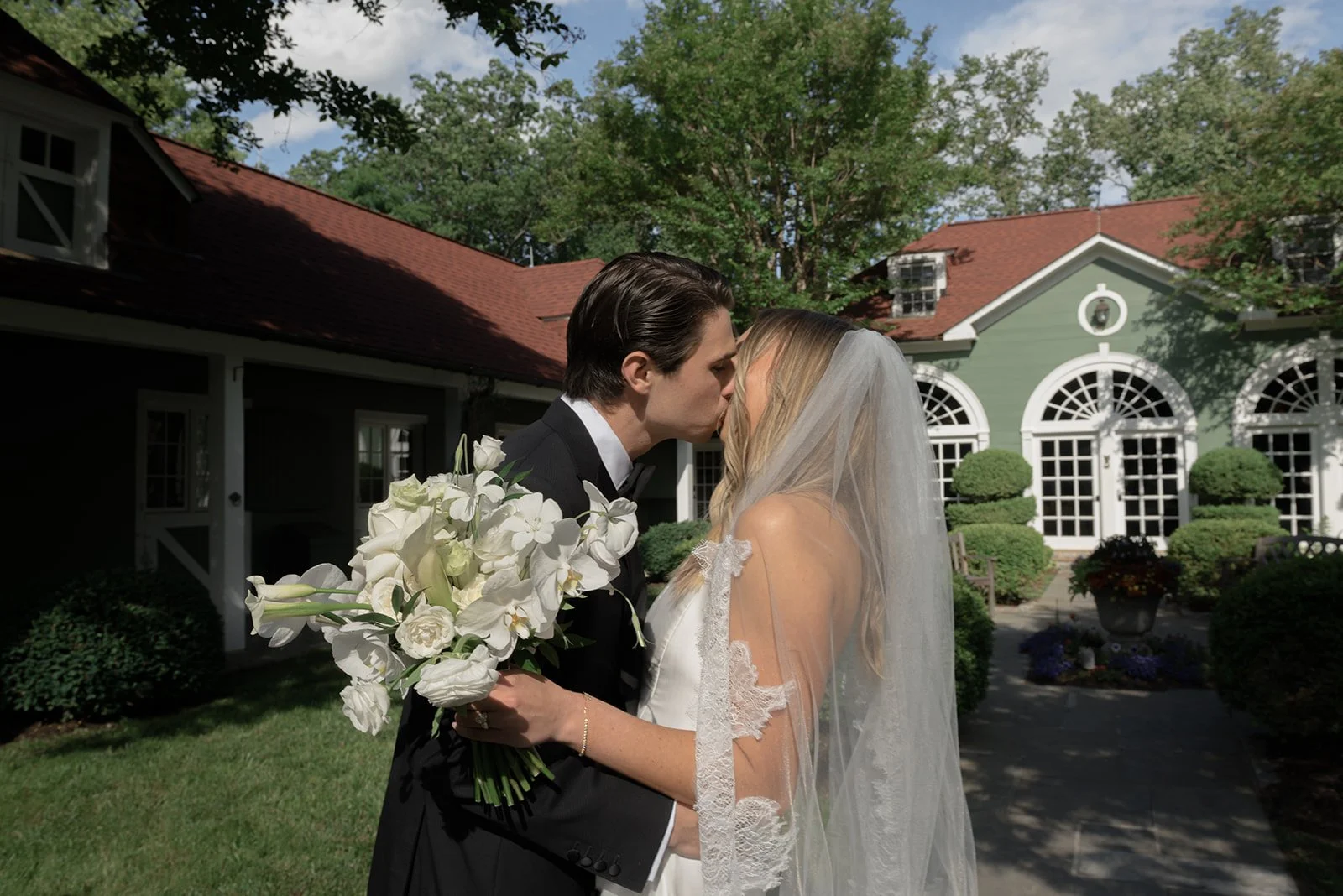 Bride and groom kissing outside the historic Carriage House at Goodstone Inn with white flowers in the foreground.