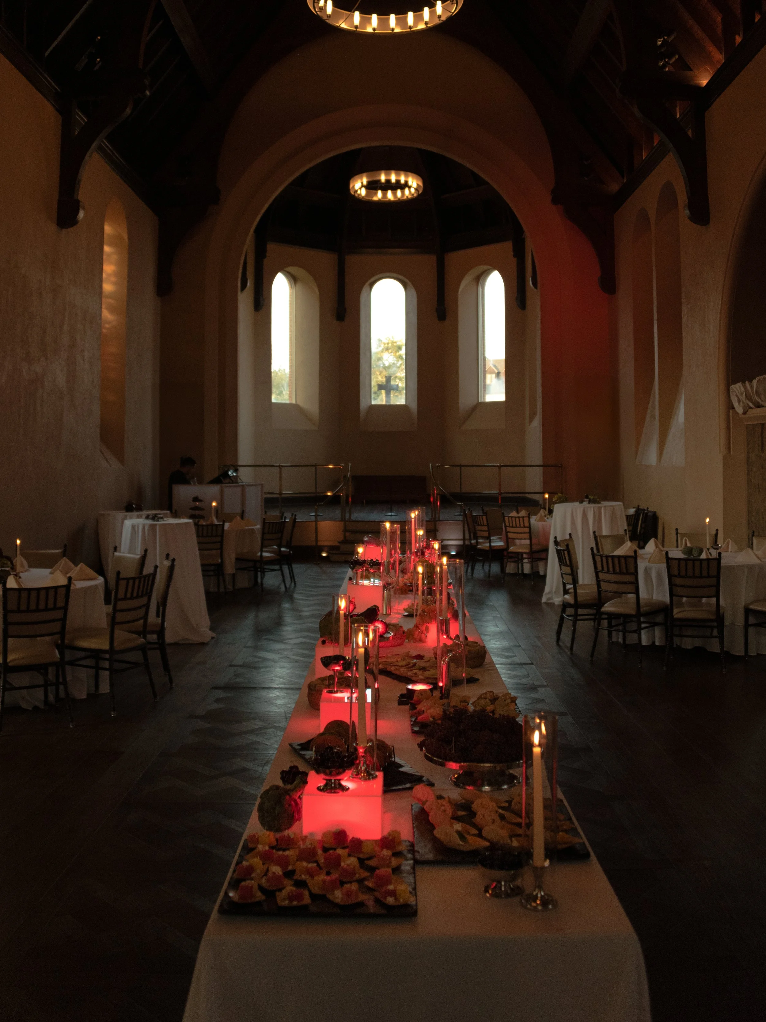 Rehearsal dinner room transformed with dramatic red candlelight and food displays.